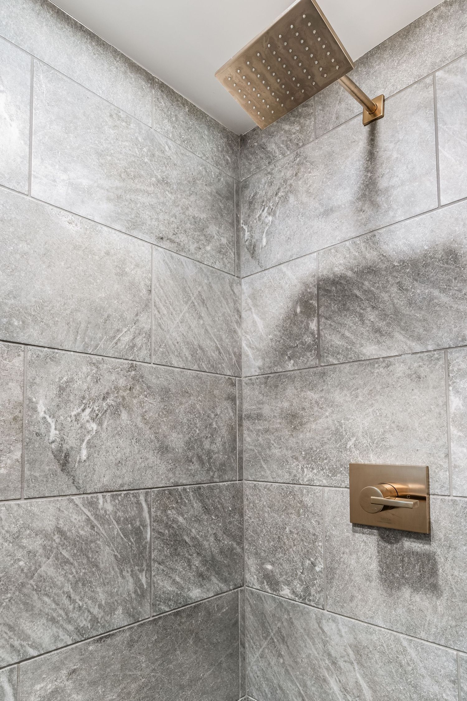 Modern shower with large gray marble tiles and brushed gold rain showerhead and control fixture.