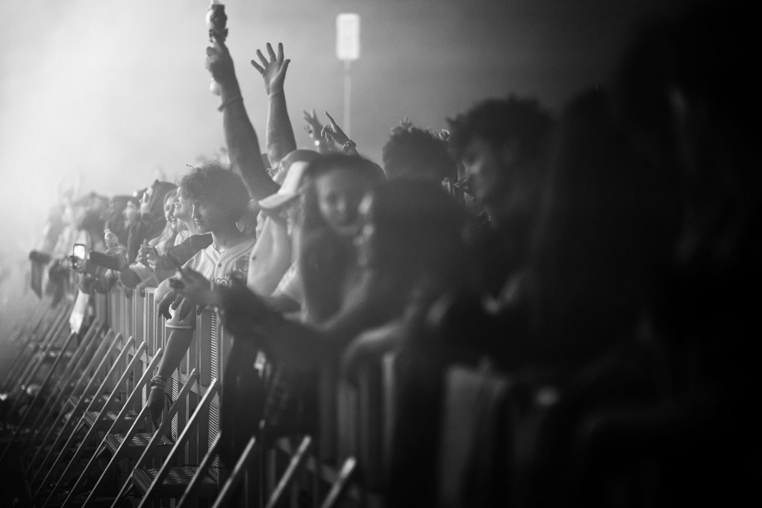 Black and white photo of energetic concert crowd pressing against metal barriers, hands raised in excitement.