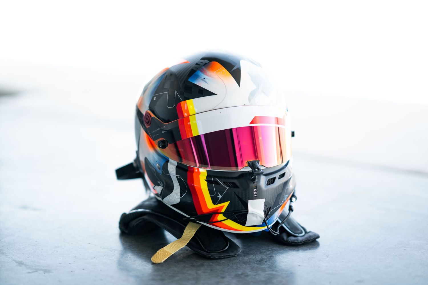 Racing helmets in vibrant colors and designs arranged in a row against a light background.