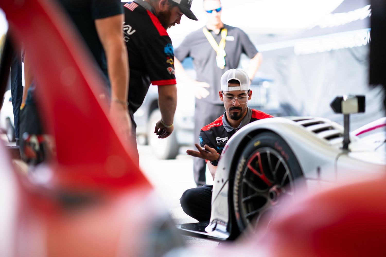 Race car mechanics making final adjustments to the vehicle during a pit stop.