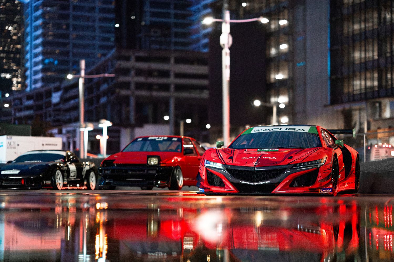 A row of luxury sports cars illuminated by red and blue lights on display at a nighttime auto show.