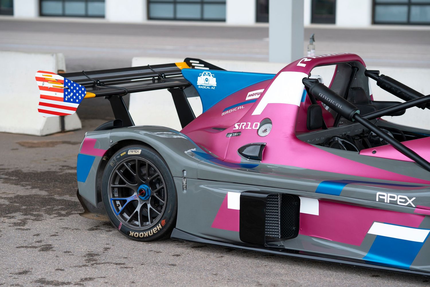 Close-up view of a modern racing car with pink and blue livery featuring a large rear wing and aerodynamic components.