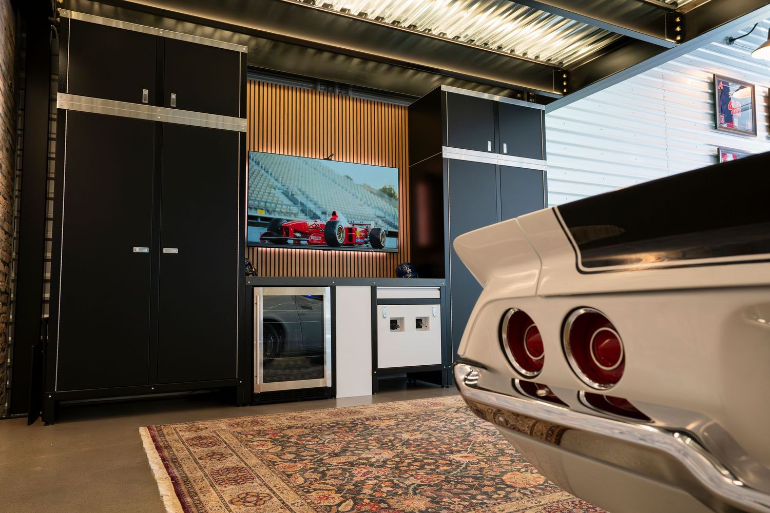 Modern garage lounge area with leather seating and entertainment system mounted on black walls.