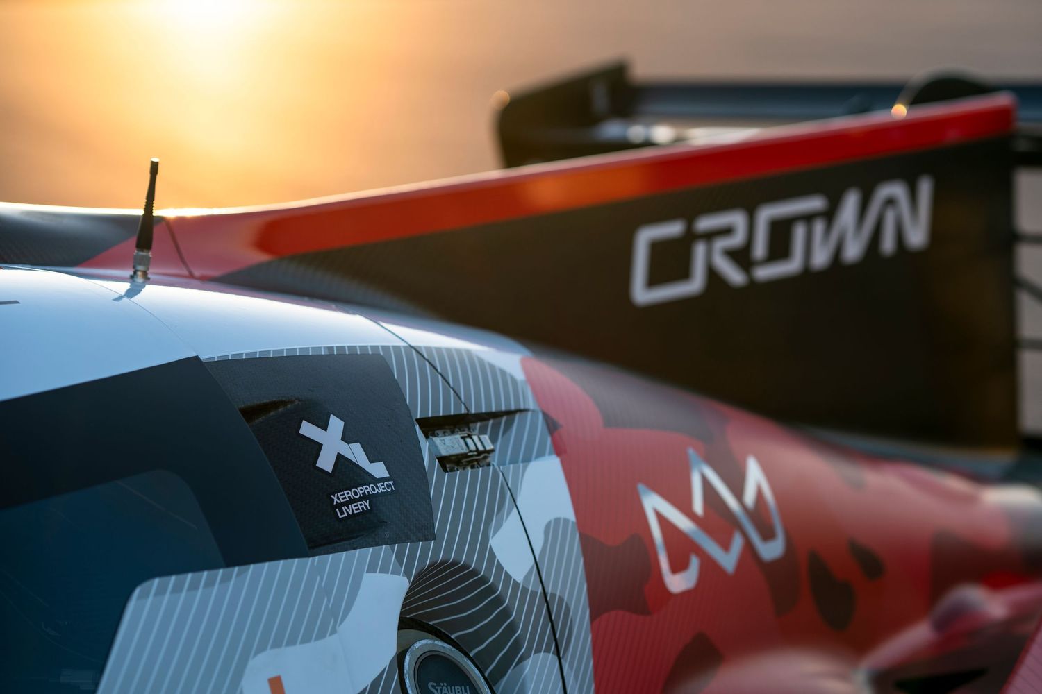Race cars silhouetted against a golden sunset with mountains in the background.