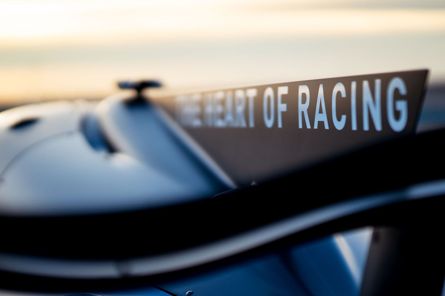 Close-up detail shot of a sleek blue racing car's exterior against a sunset sky.