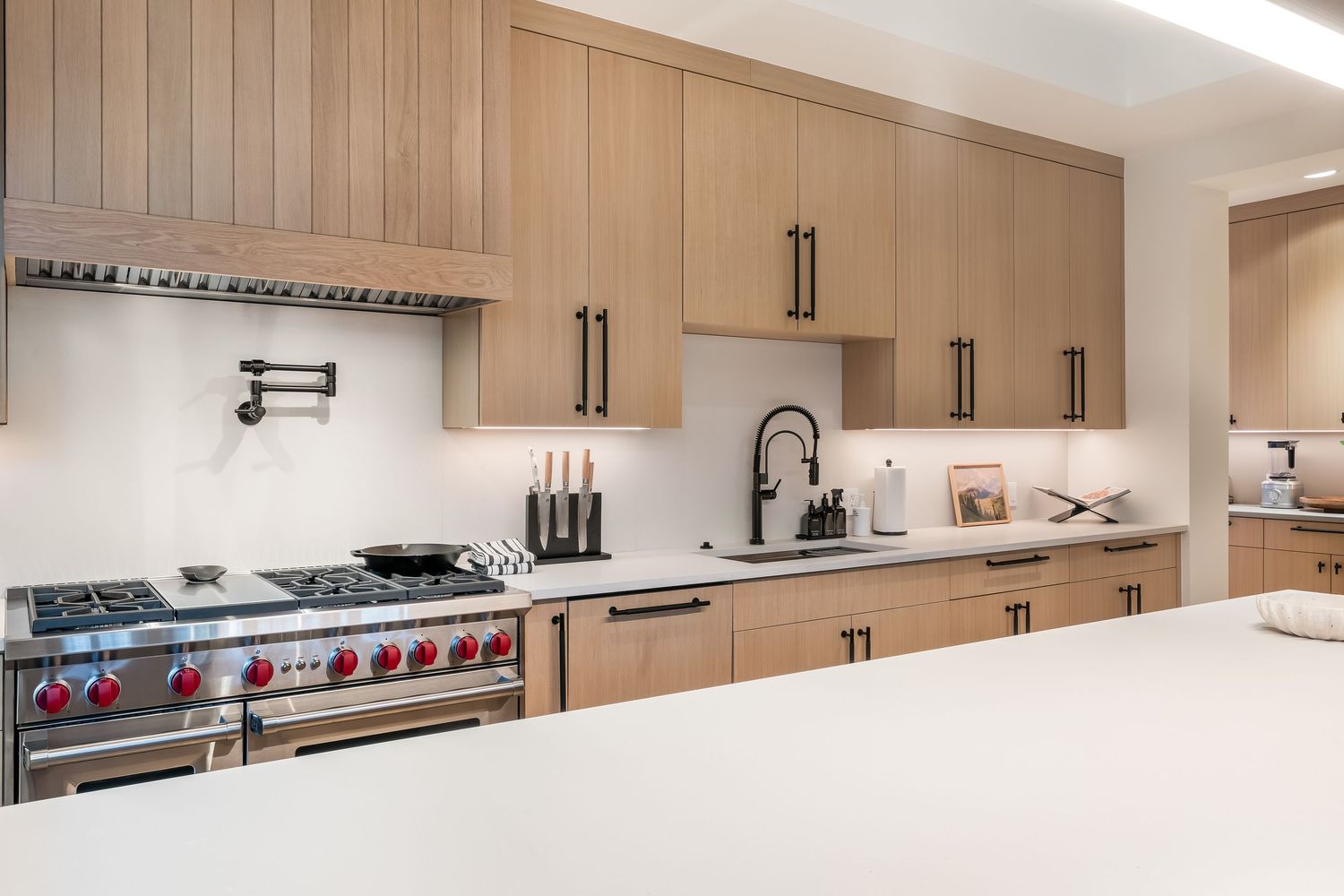 Modern beige kitchen with light wood cabinets, stainless steel appliances, and white quartz countertops in a panoramic view.
