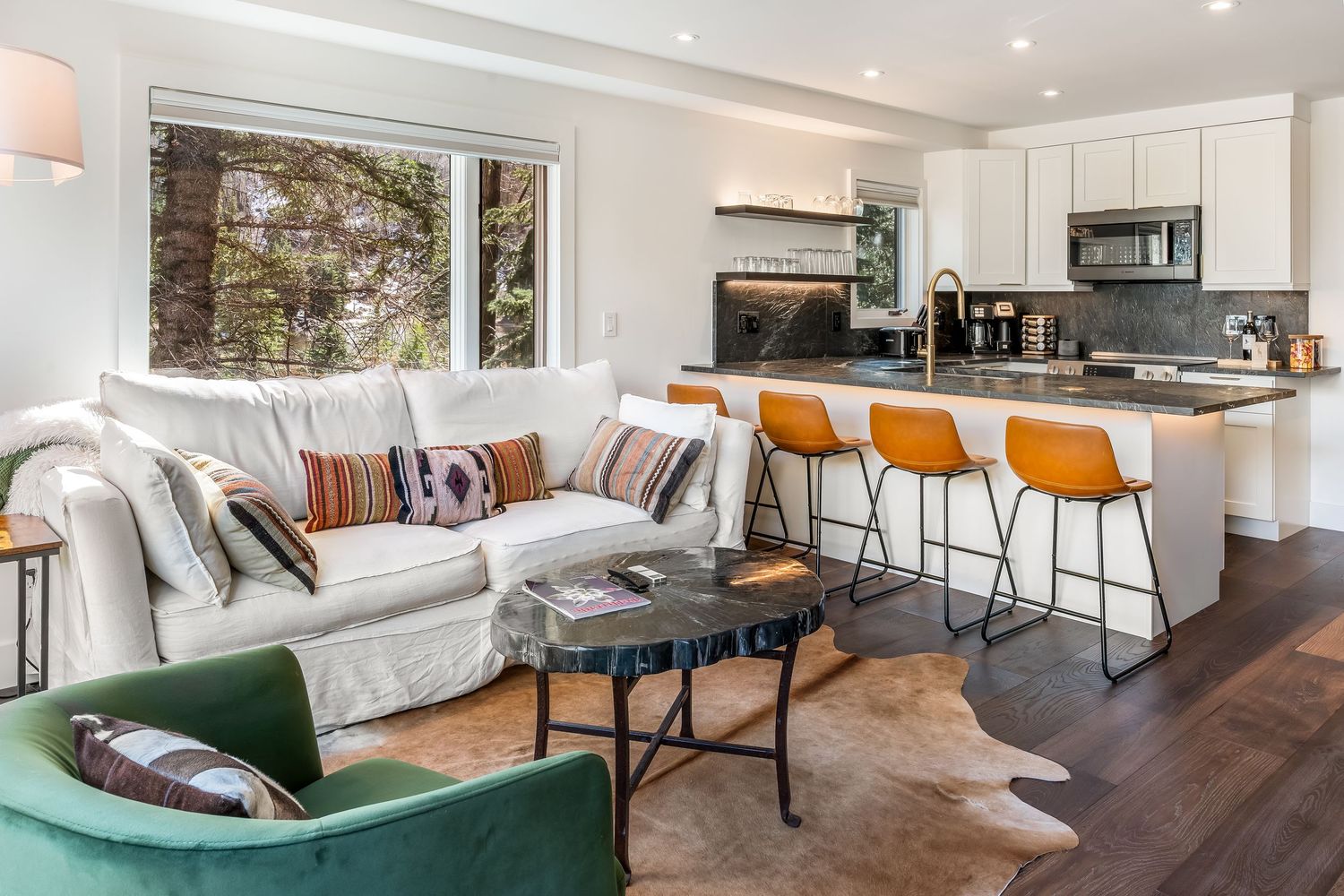 Modern open-plan living room with white sectional sofa, orange bar stools, kitchen island, and hardwood floors.