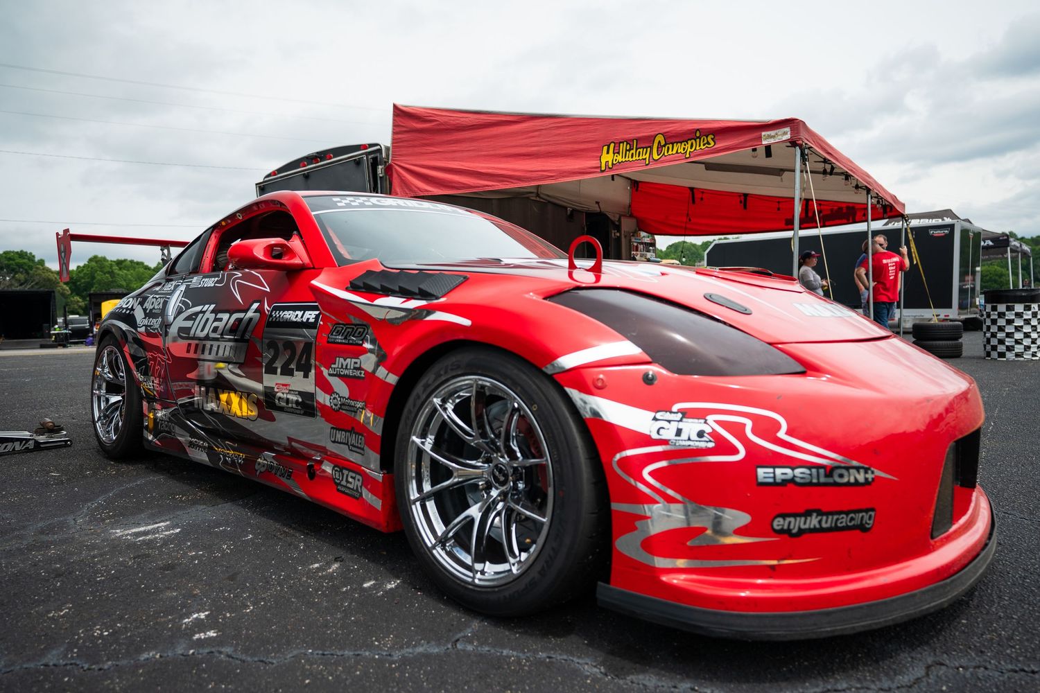 Red Nissan 350Z drift car with sponsor decals parked at a Formula Drift racing event.