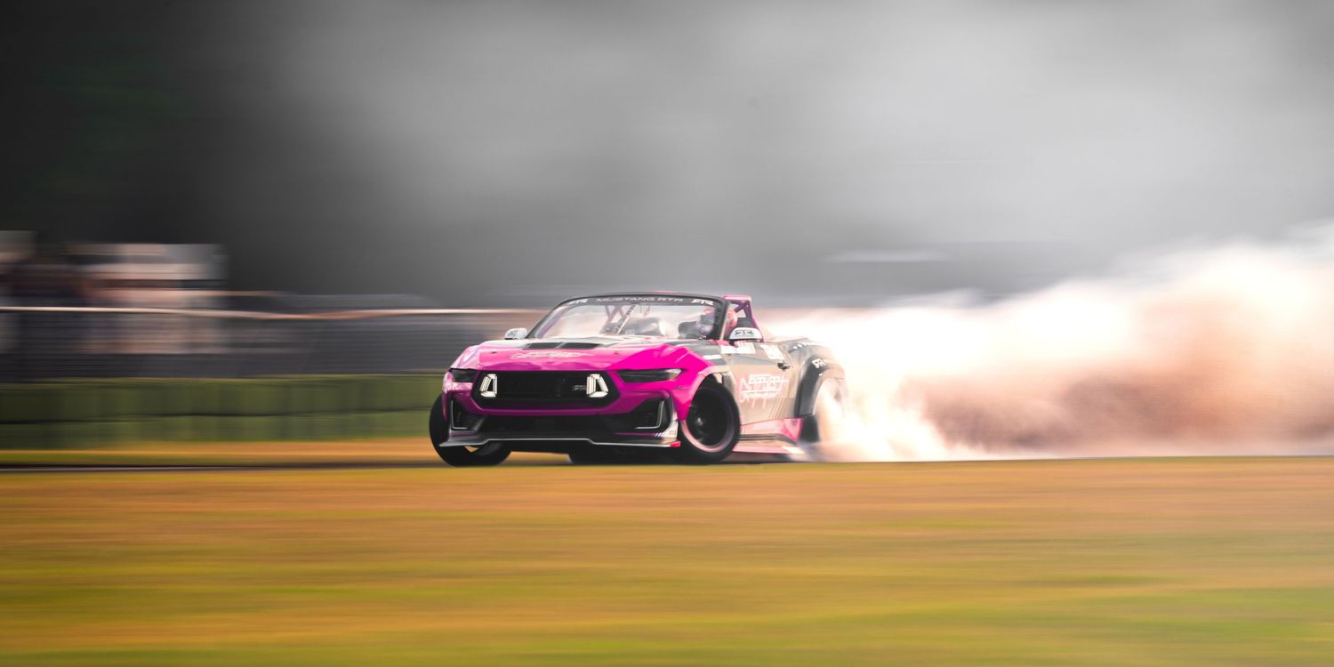 Pink drift car spinning tires with massive smoke cloud on a racing track during a high-speed motorsport event.
