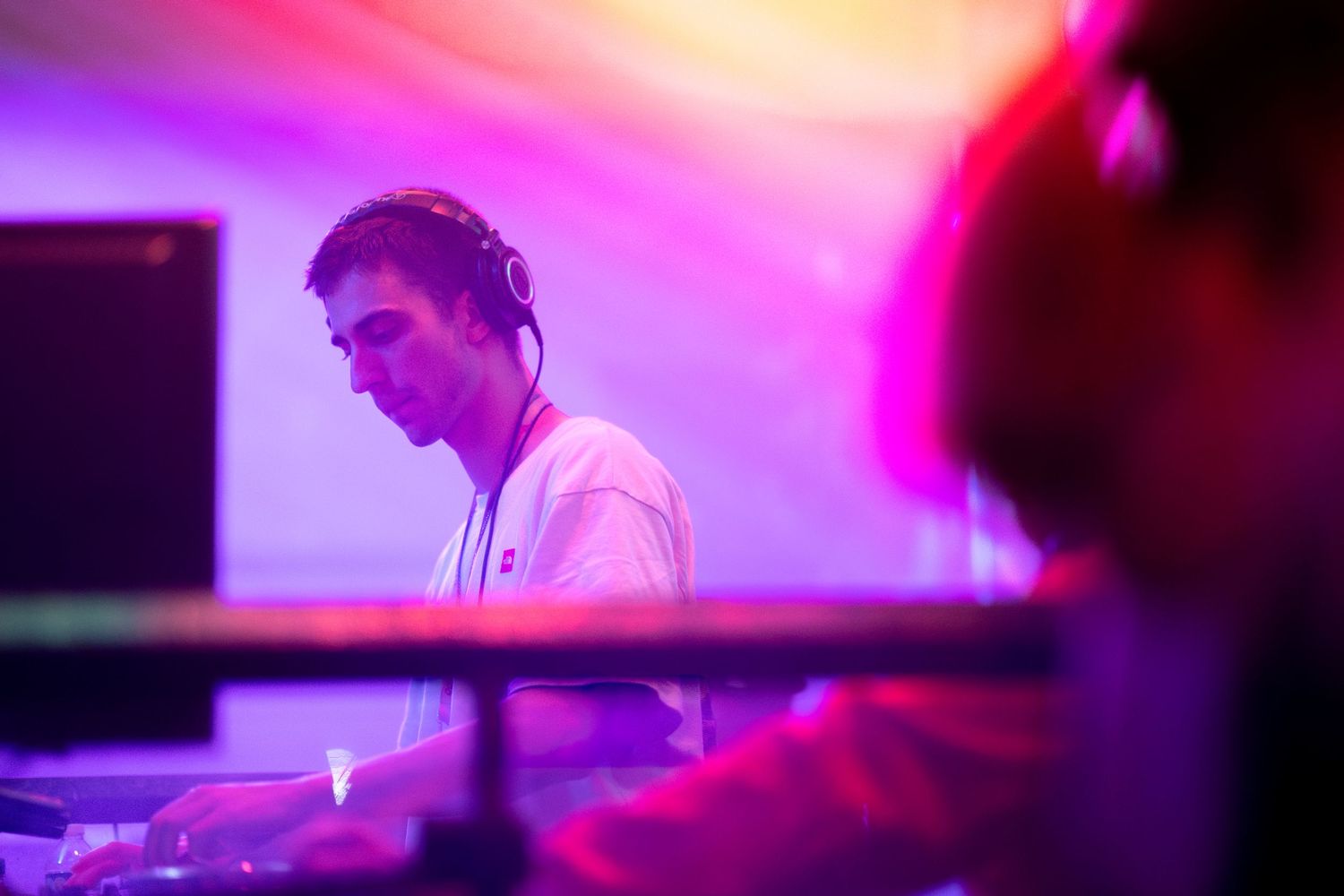 A DJ performs at a nightclub with vibrant pink and purple lighting creating an energetic atmosphere.