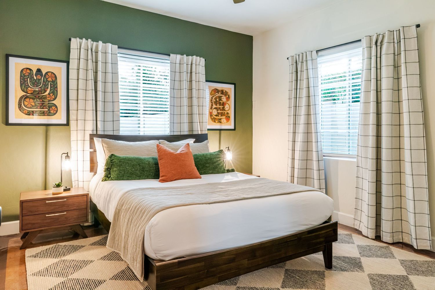 Modern apartment bedroom with green accent wall, white bedding, and natural lighting through windows.