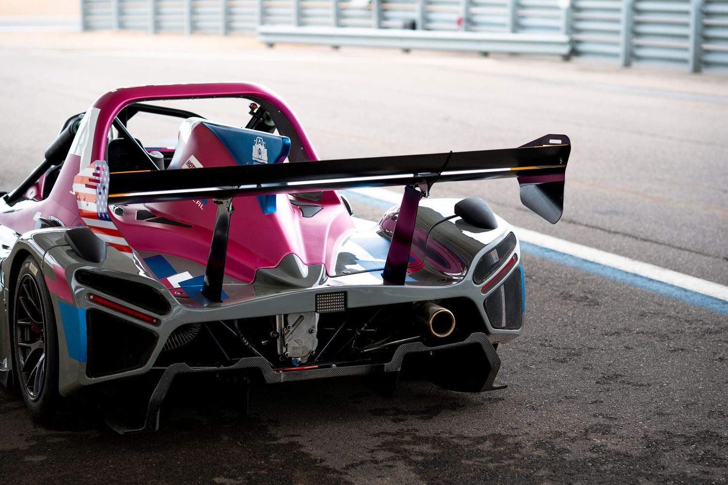 Sleek red and black racing car with aerodynamic bodywork speeds around a racetrack during competition.
