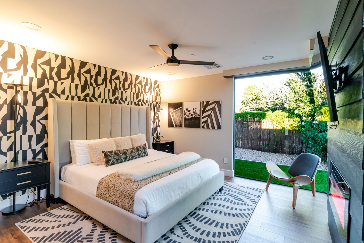 Modern bedroom with black and white geometric wall art, plush white bed, and glass doors opening to outdoor patio.
