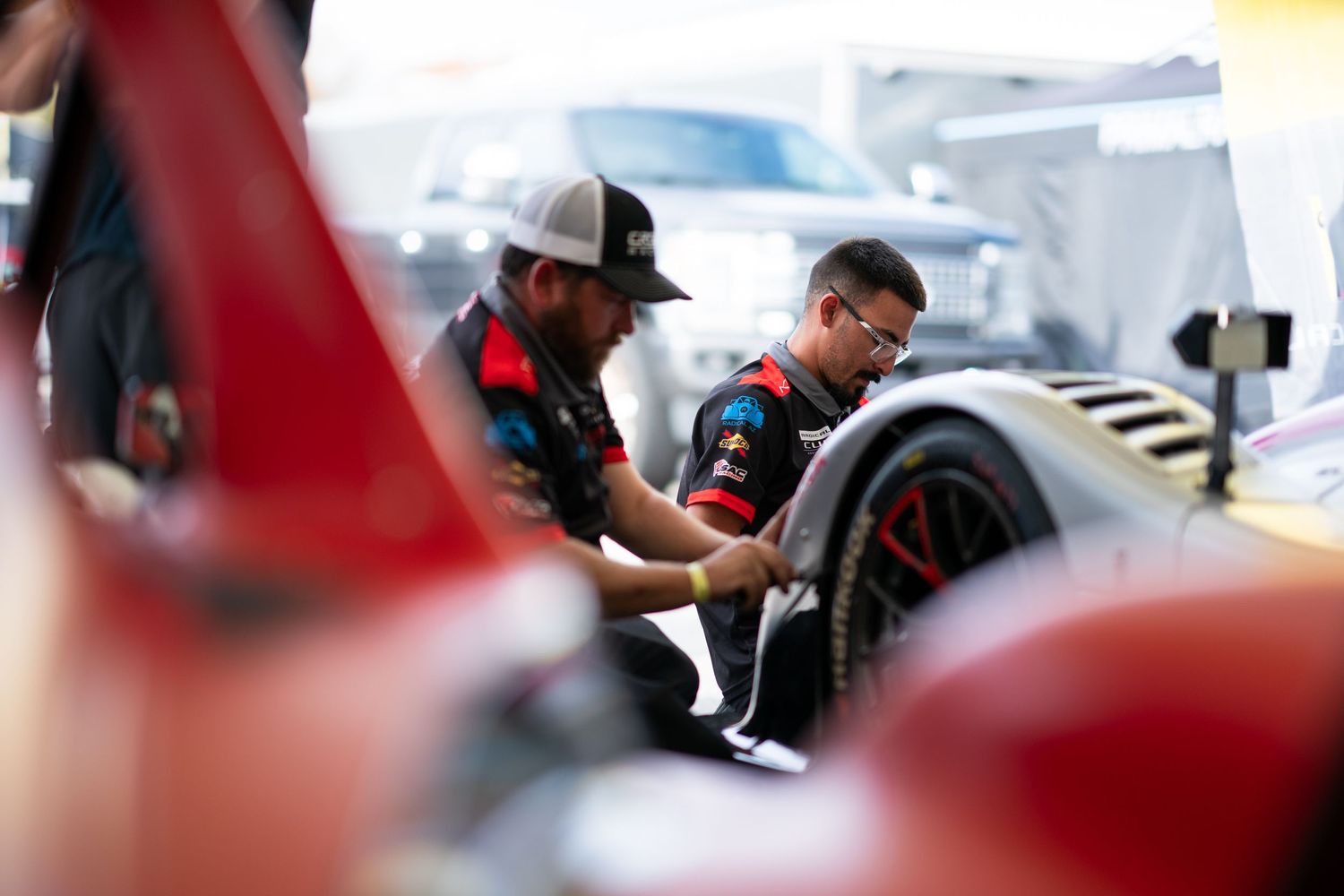 Racing team members collaborating in the pit lane during a motorsport event.
