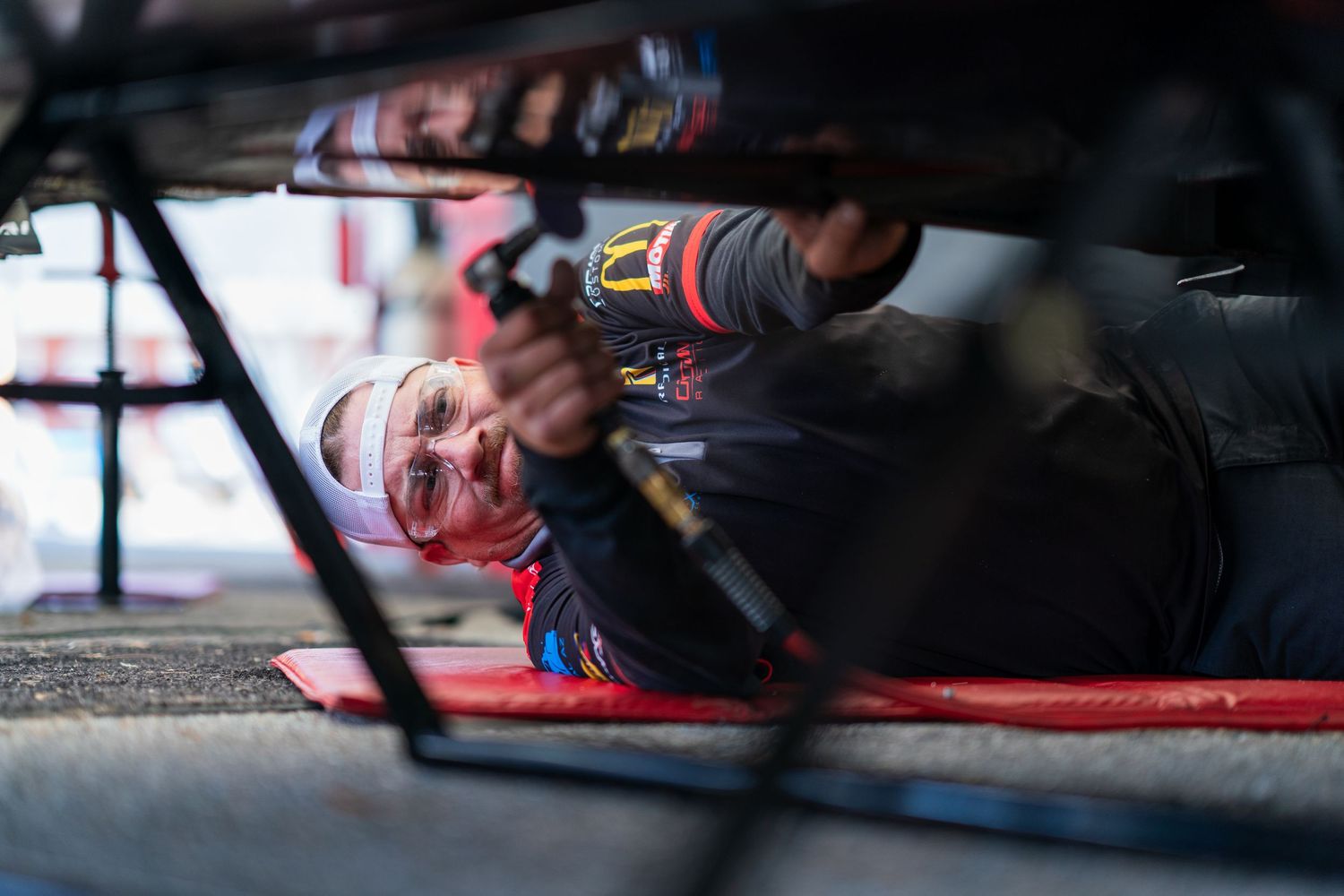 Close-up shot of race car mechanics working underneath a vehicle during maintenance.