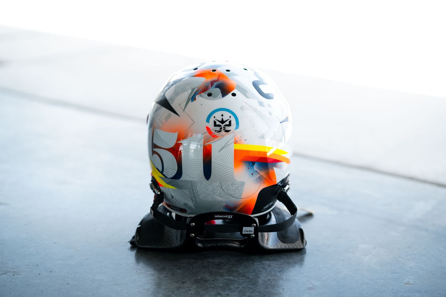 Motorsport helmet featuring grey base color with orange geometric patterns.