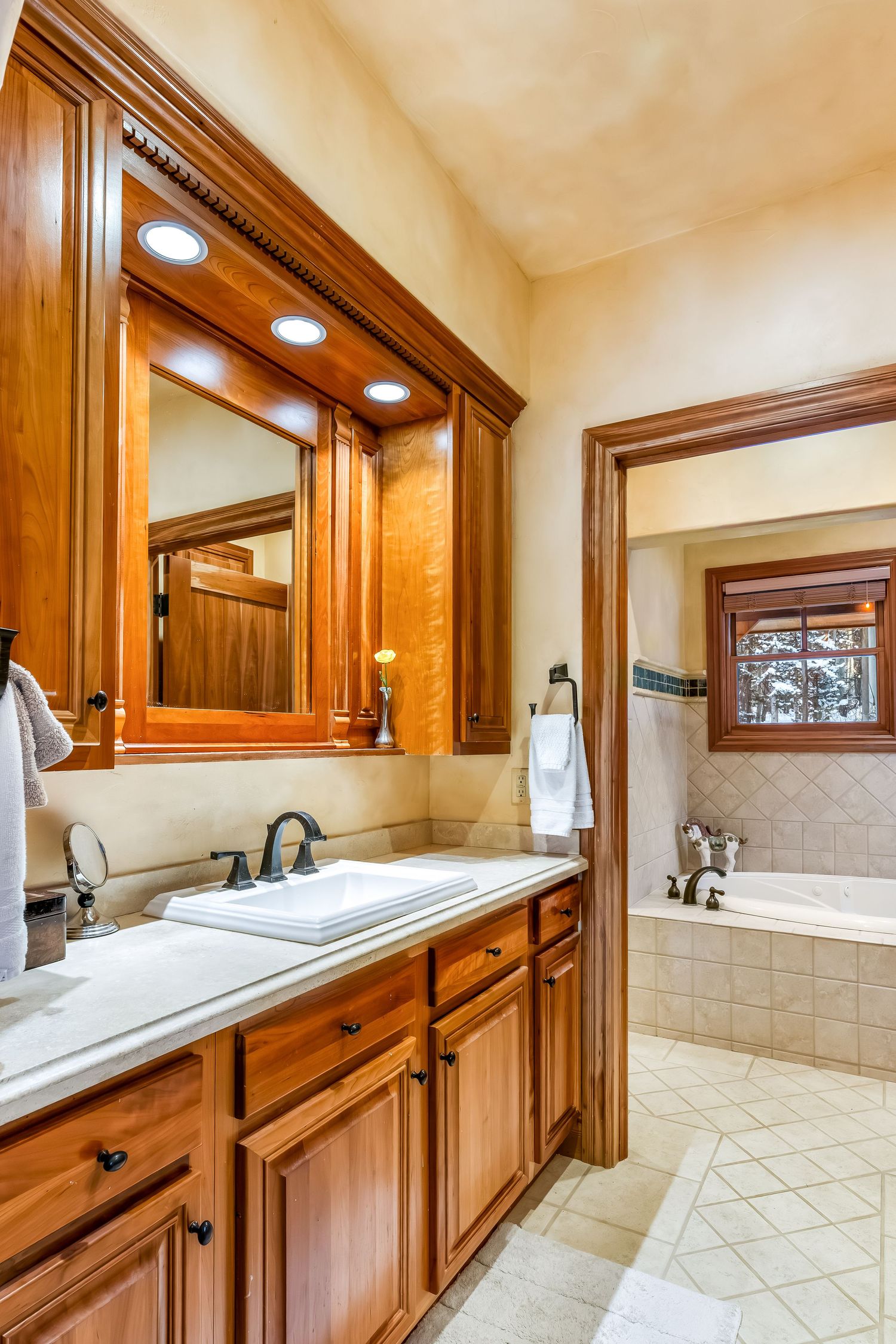 Luxurious bathroom interior featuring rich wooden cabinetry and cream-colored tile with multiple vanity sections.