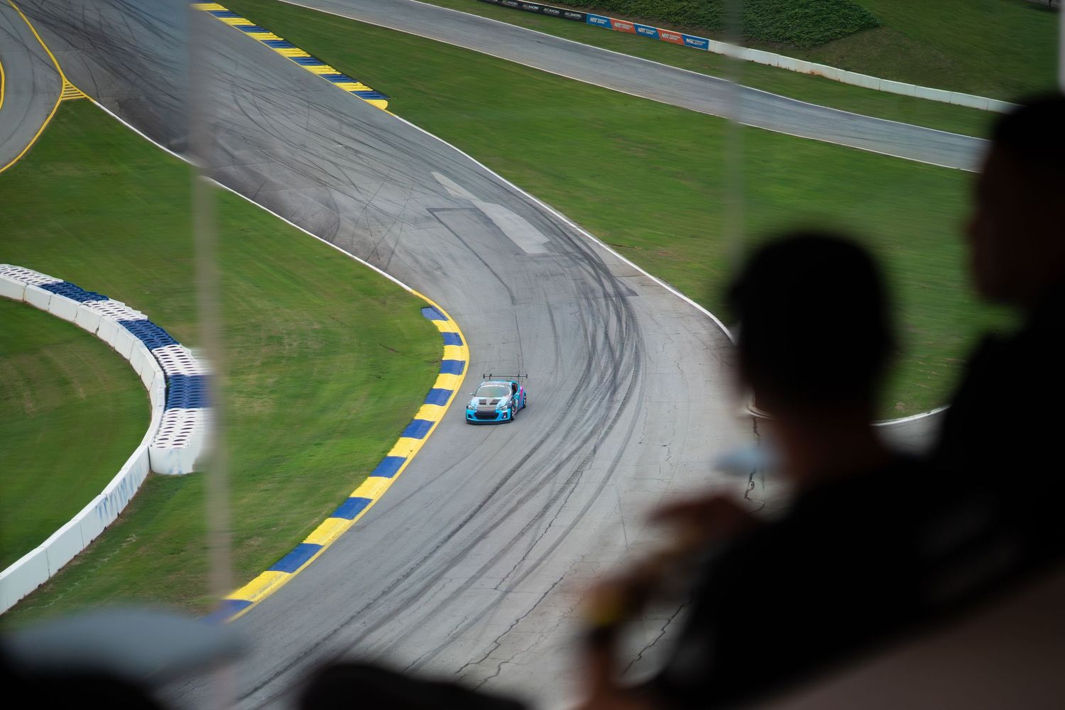 Aerial view of a race car navigating a curved track while spectators watch from above.