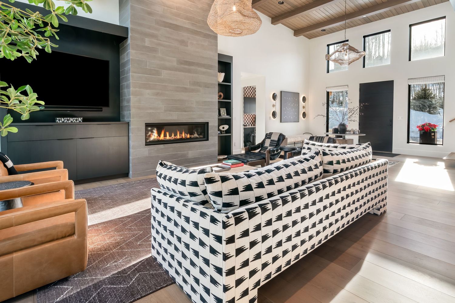 Modern living room features a black and white geometric ottoman beside a tan leather sofa and sleek fireplace.