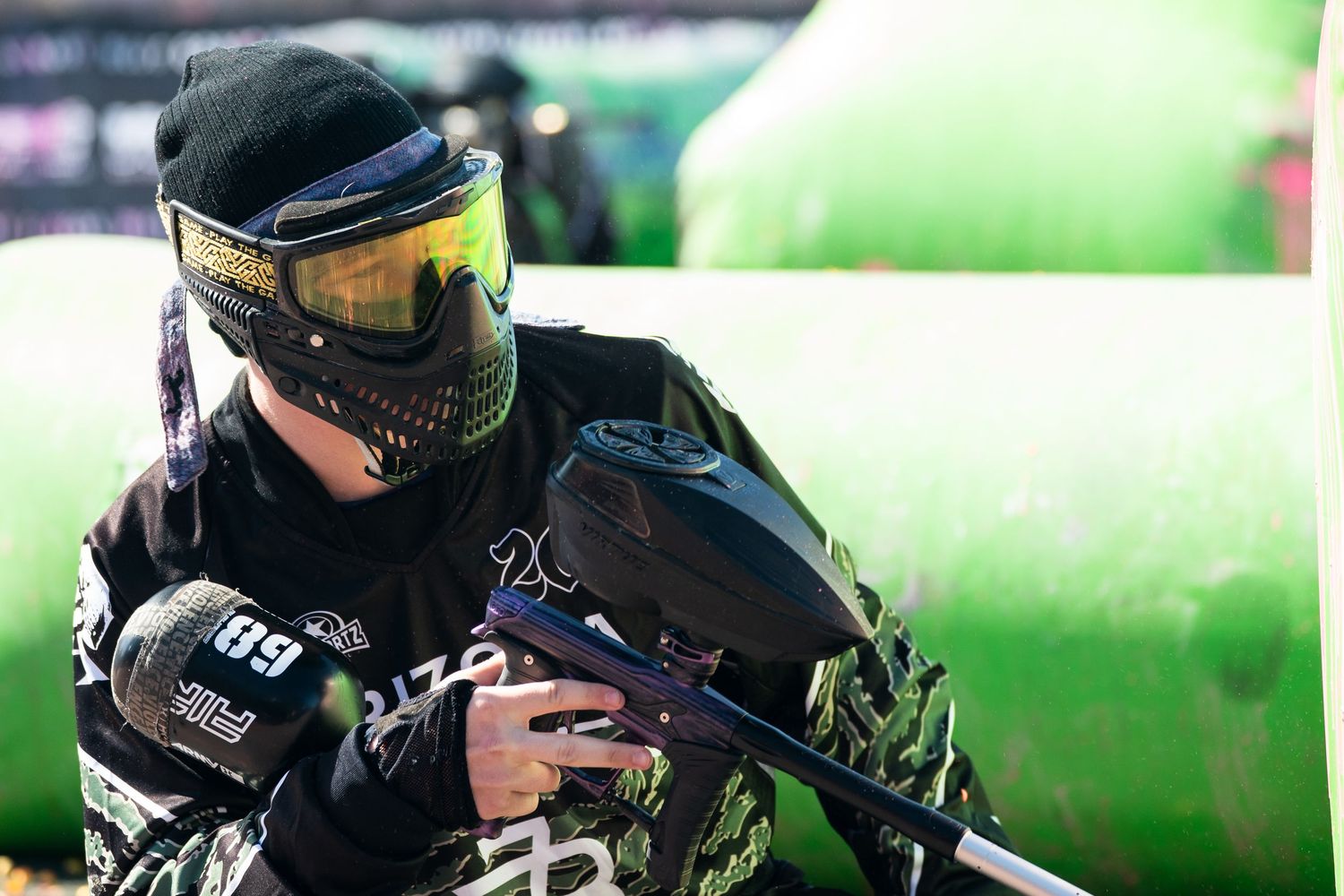 A paintball player in camouflage gear and protective mask aims their marker during an outdoor tournament game.
