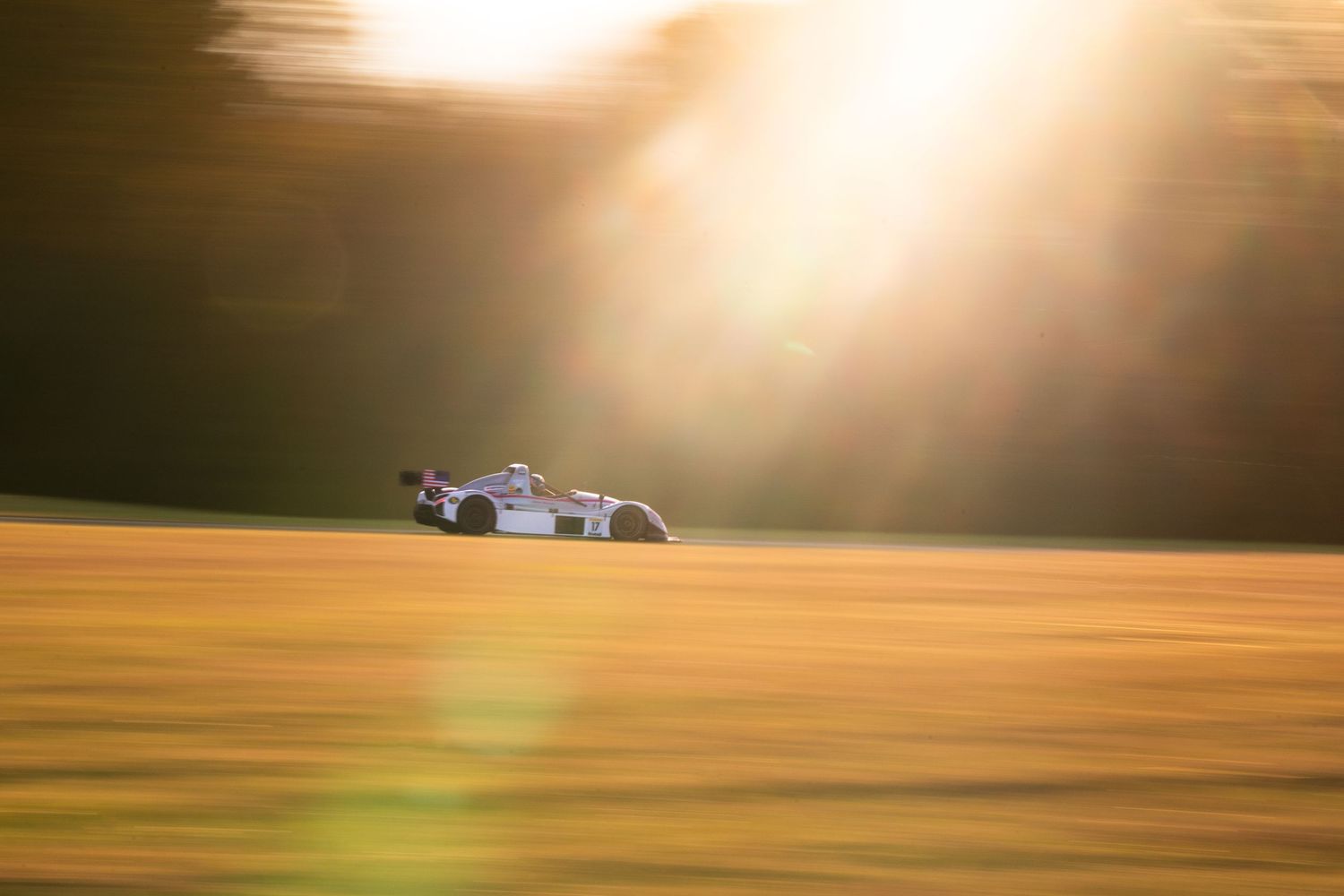 Race cars speeding past on track during golden hour with dramatic sunlight.