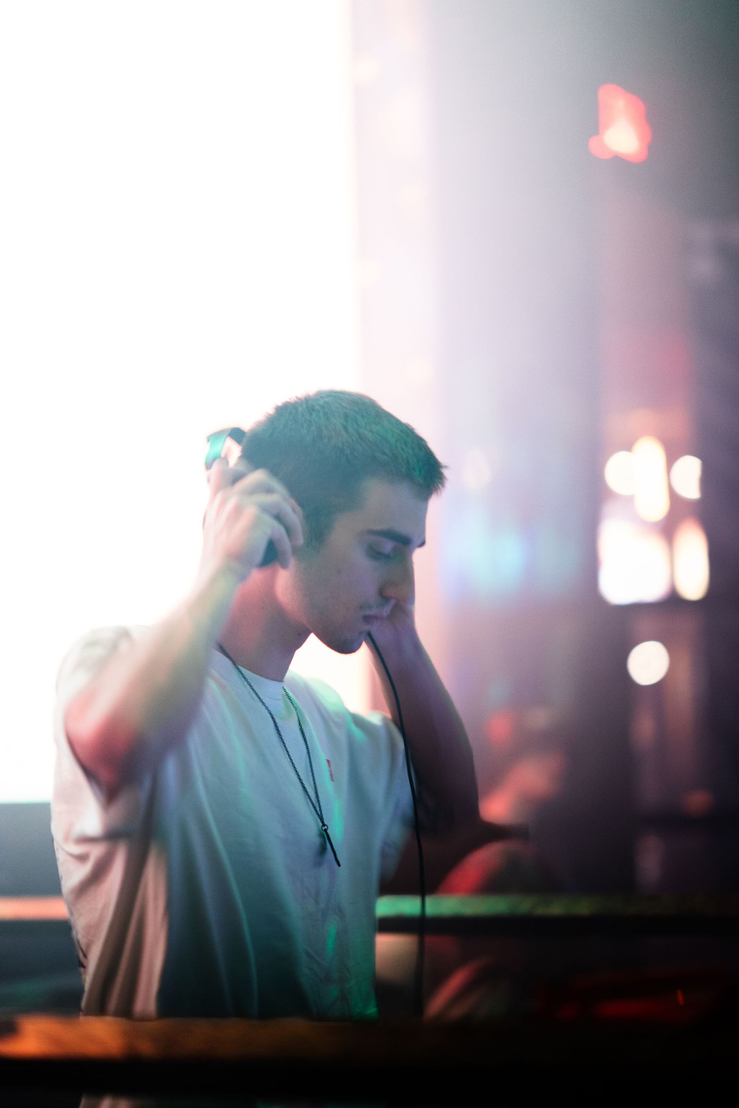 DJ performing at a nightclub with atmospheric lighting and bokeh effects in the background.