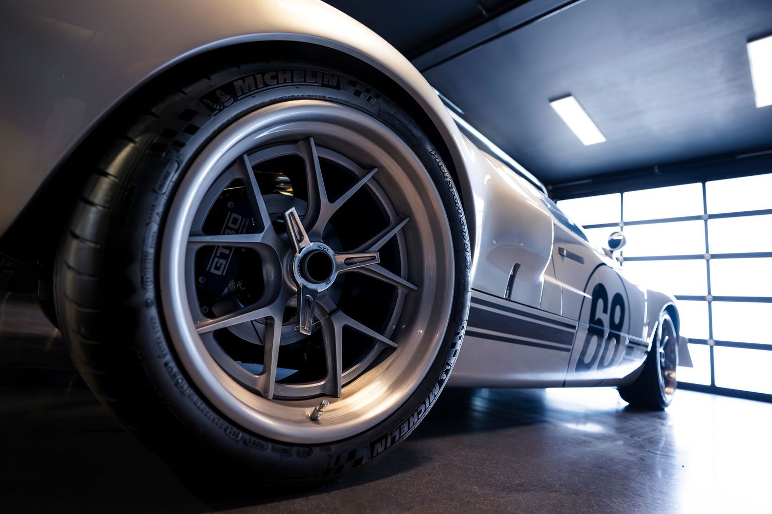 Close-up view of sleek sports car wheels and rims against dramatic lighting in a garage setting.