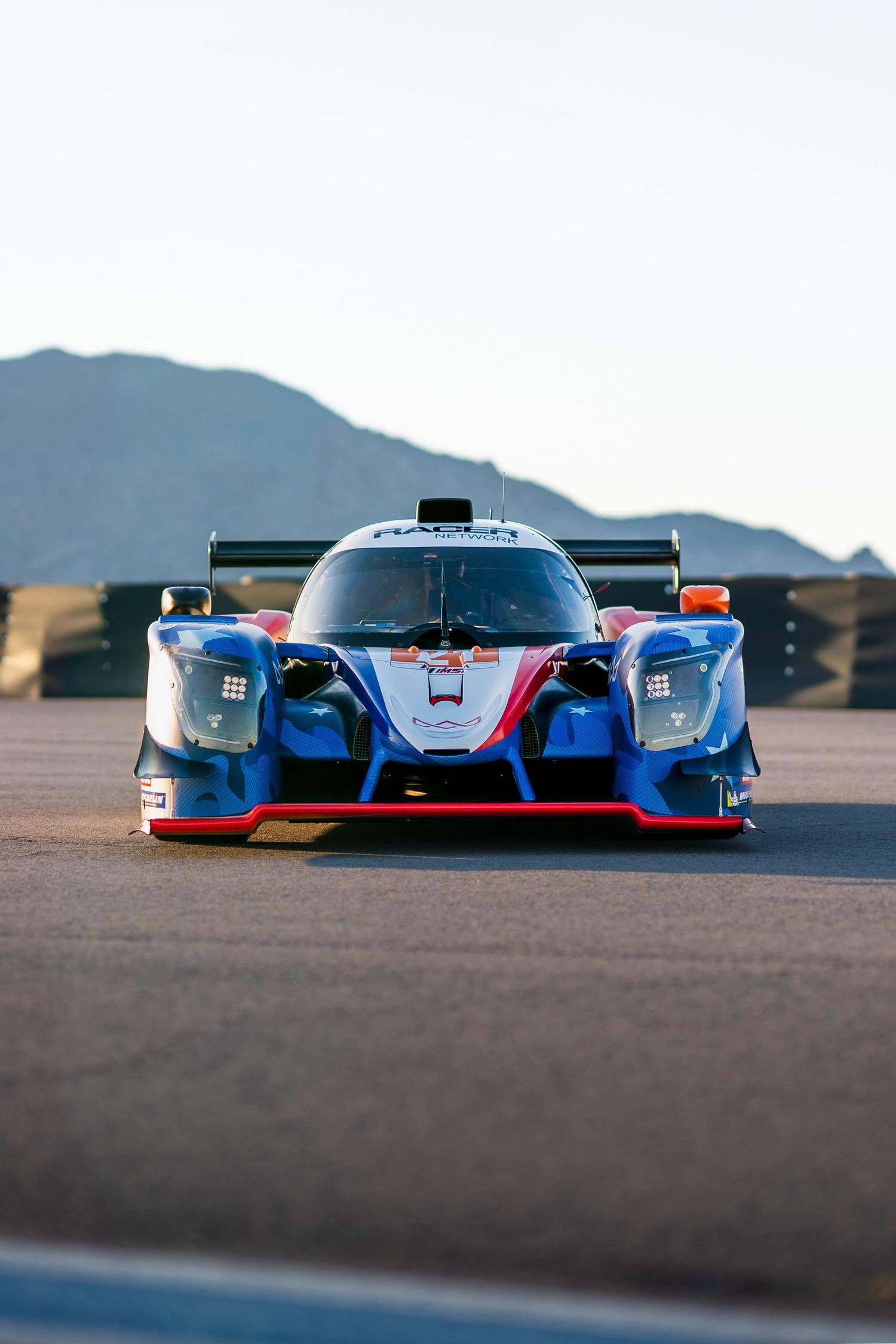 Three prototype race cars positioned on a desert racing circuit with mountain backdrop.