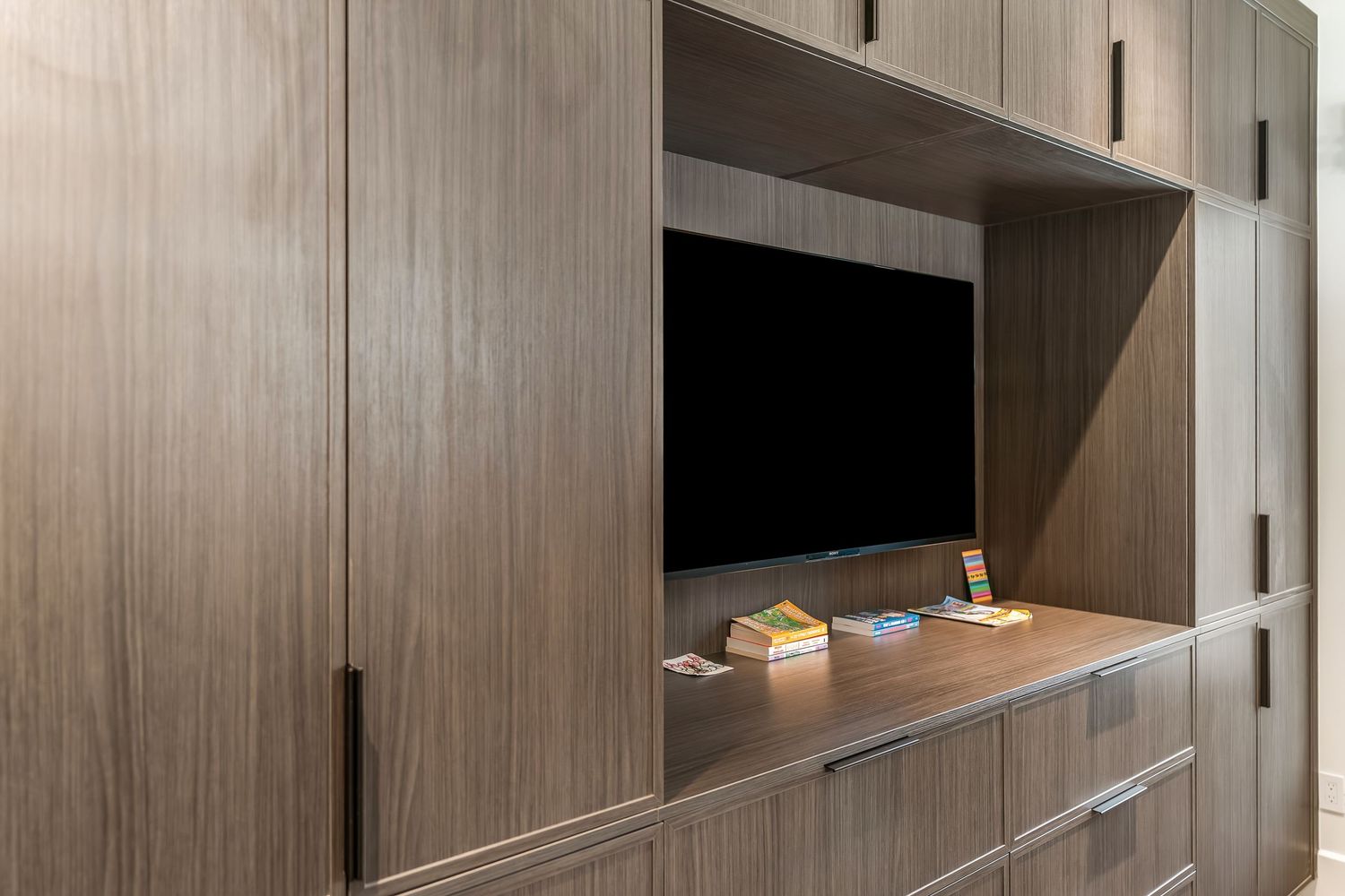 Modern kitchen cabinets with wood grain finish and sleek hardware extend along a minimalist wall design.