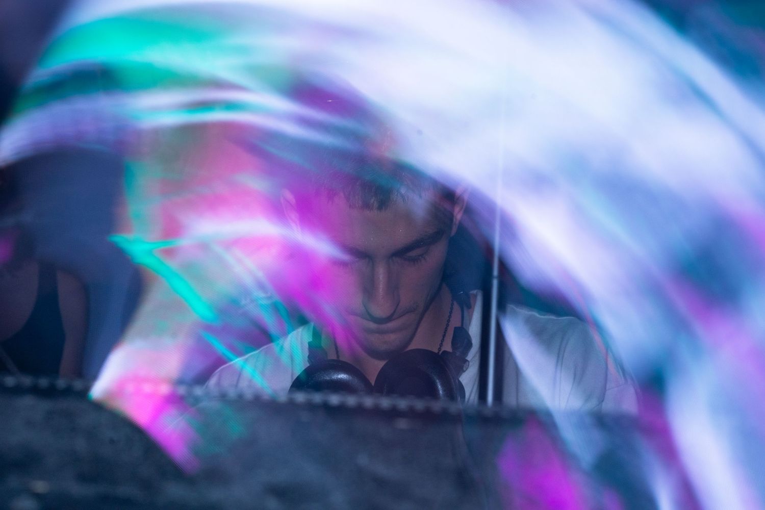 Abstract light trails in neon blue and pink colors create a dynamic swirling motion effect against a dark background.