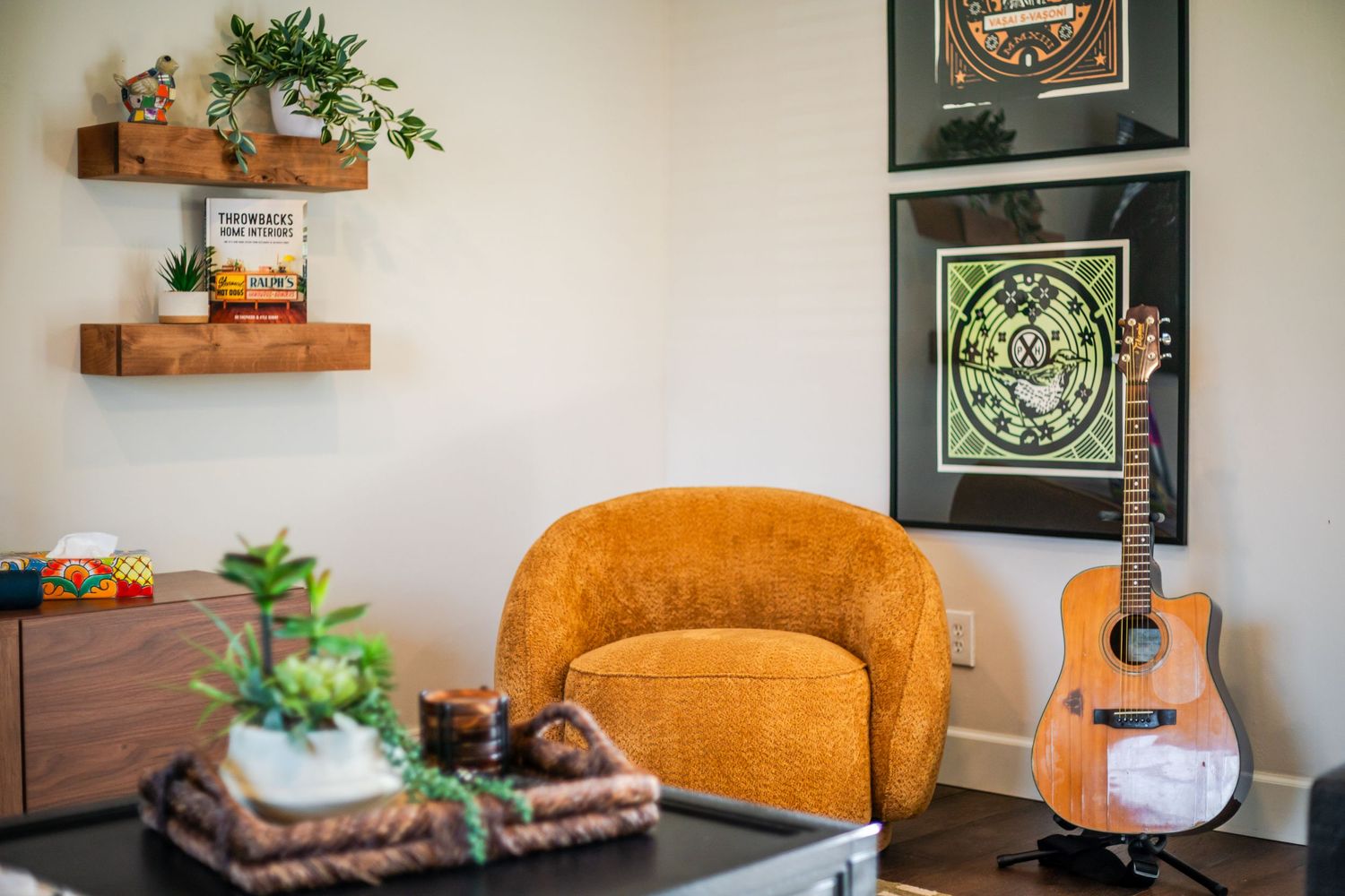 Living space with orange accent chair, wall art, and decorative plants on floating shelves.