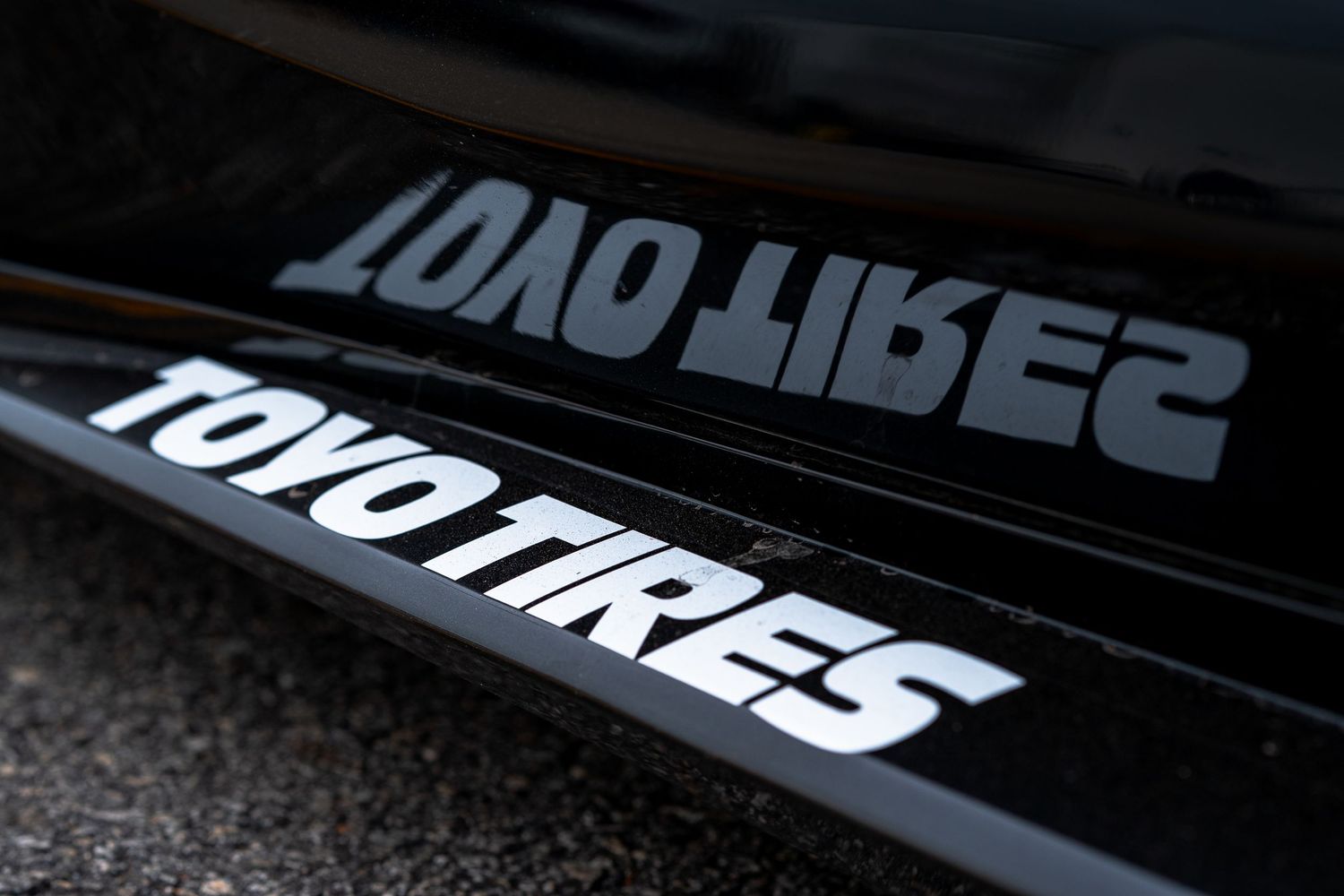 Toyo Tires decal reflected on glossy black car surface at racing event.