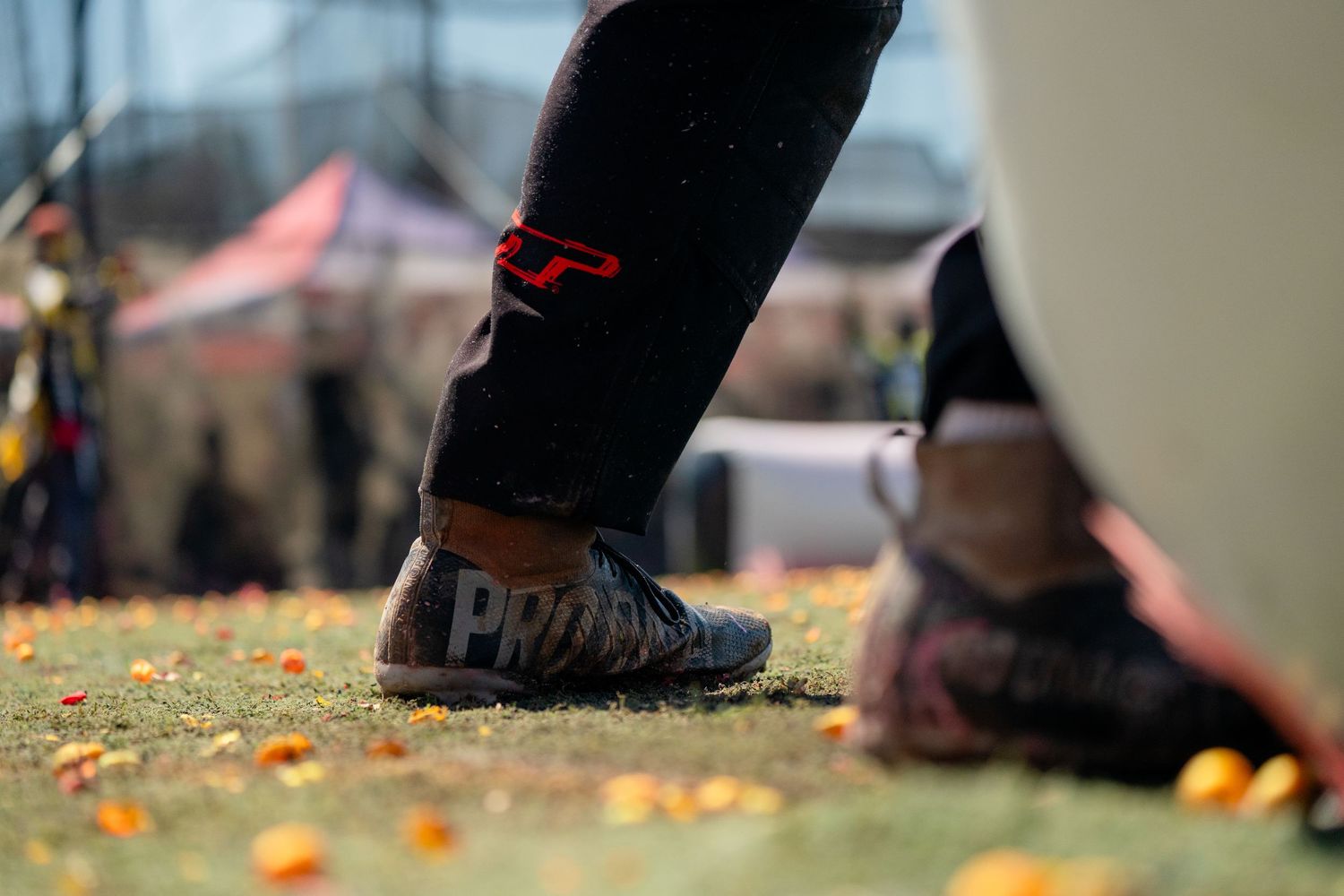 Close-up of paintball player's legs in black pants and athletic shoes on field.