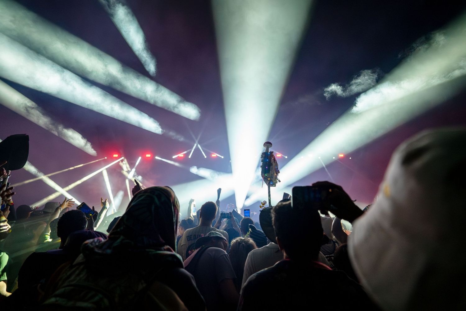 Crowd at a live concert with dramatic light beams illuminating a performer on stage in a dark venue.