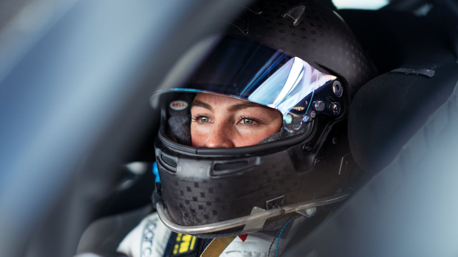 Racing driver wearing helmet inside vehicle cockpit during track session.