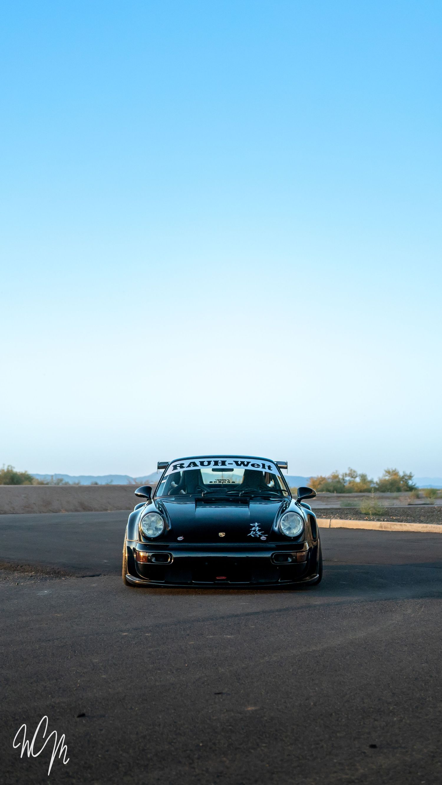 Front view of black modified Porsche 911 with RWB body kit against blue sky.