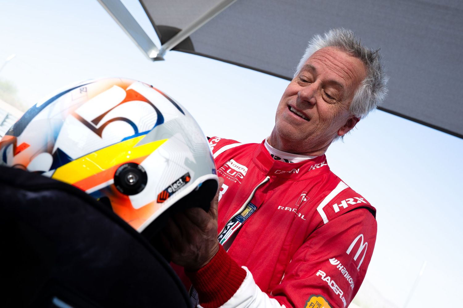 Racing driver in red suit makes adjustments to a Formula 1 car during pit stop preparations.
