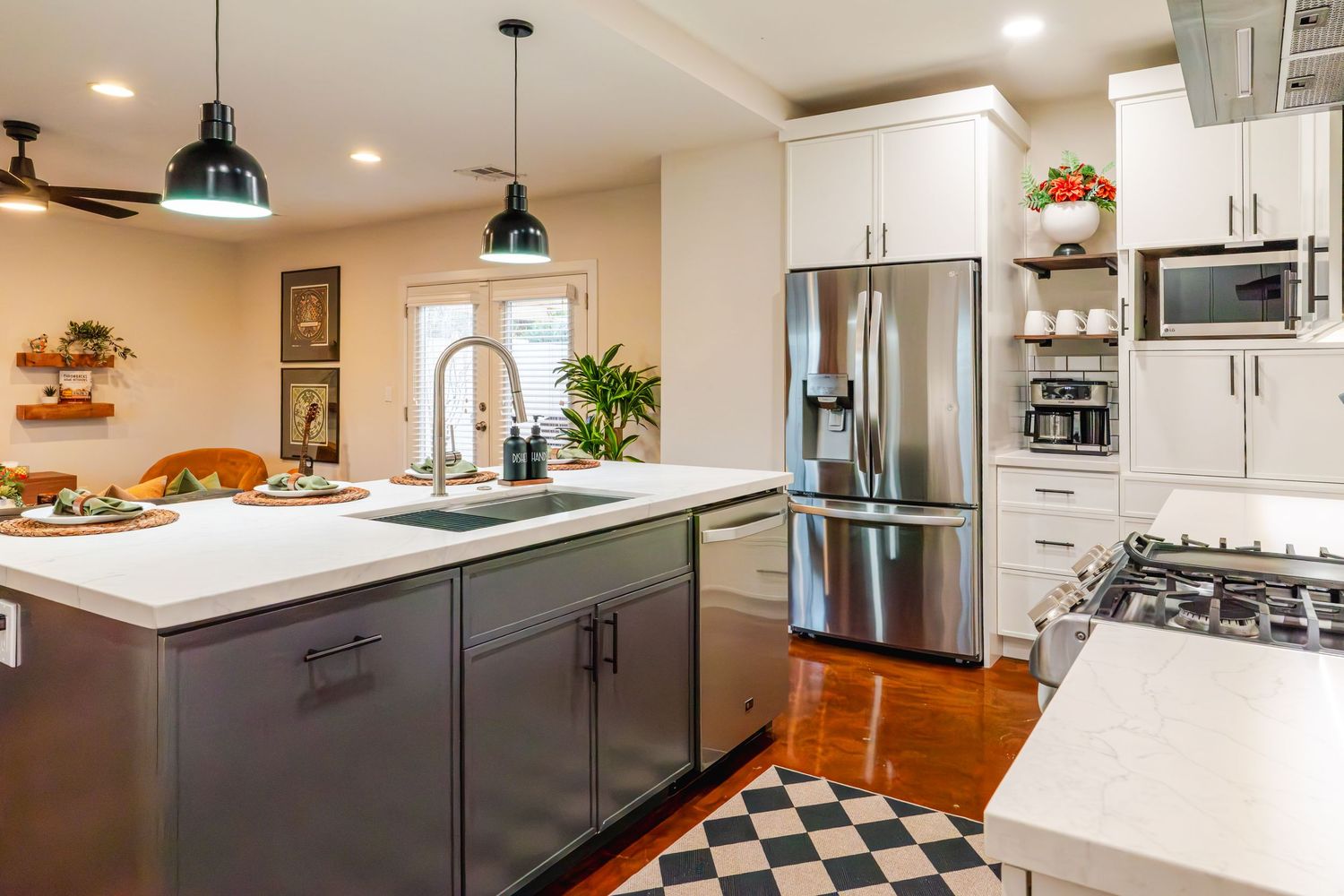 Modern kitchen with white cabinets, dark gray island, stainless appliances and checkered floor tiles.