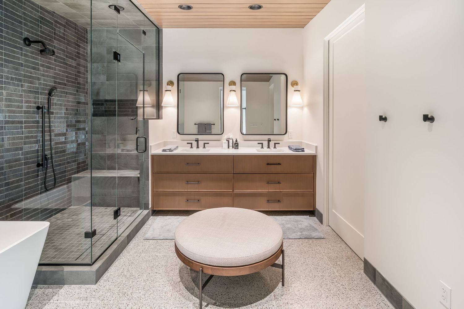 Luxurious bathroom with glass shower enclosure, grey tile walls, and wooden ceiling accents.