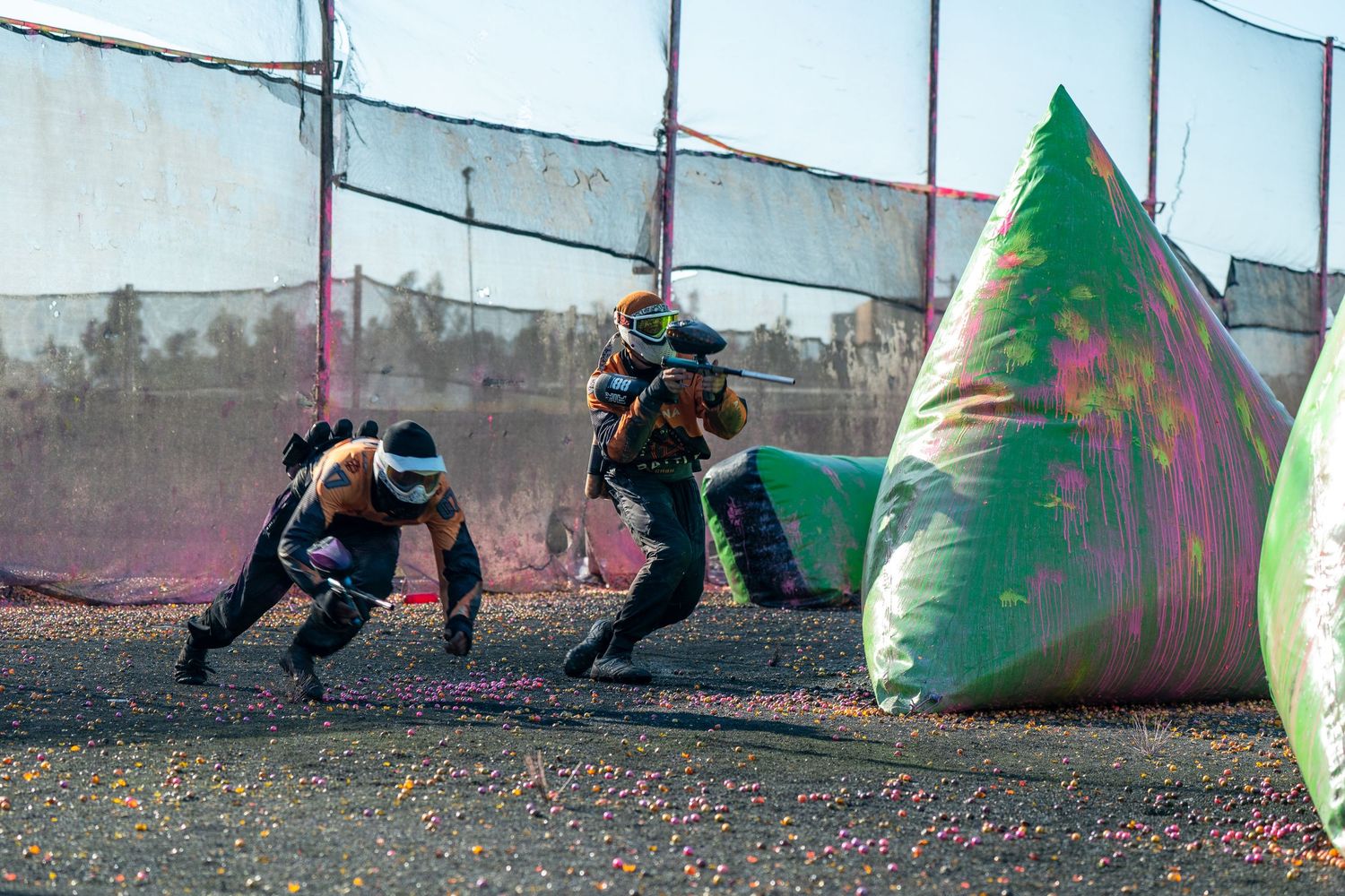 Two paintball players sprint behind a colorful inflatable bunker during a competitive outdoor paintball match.