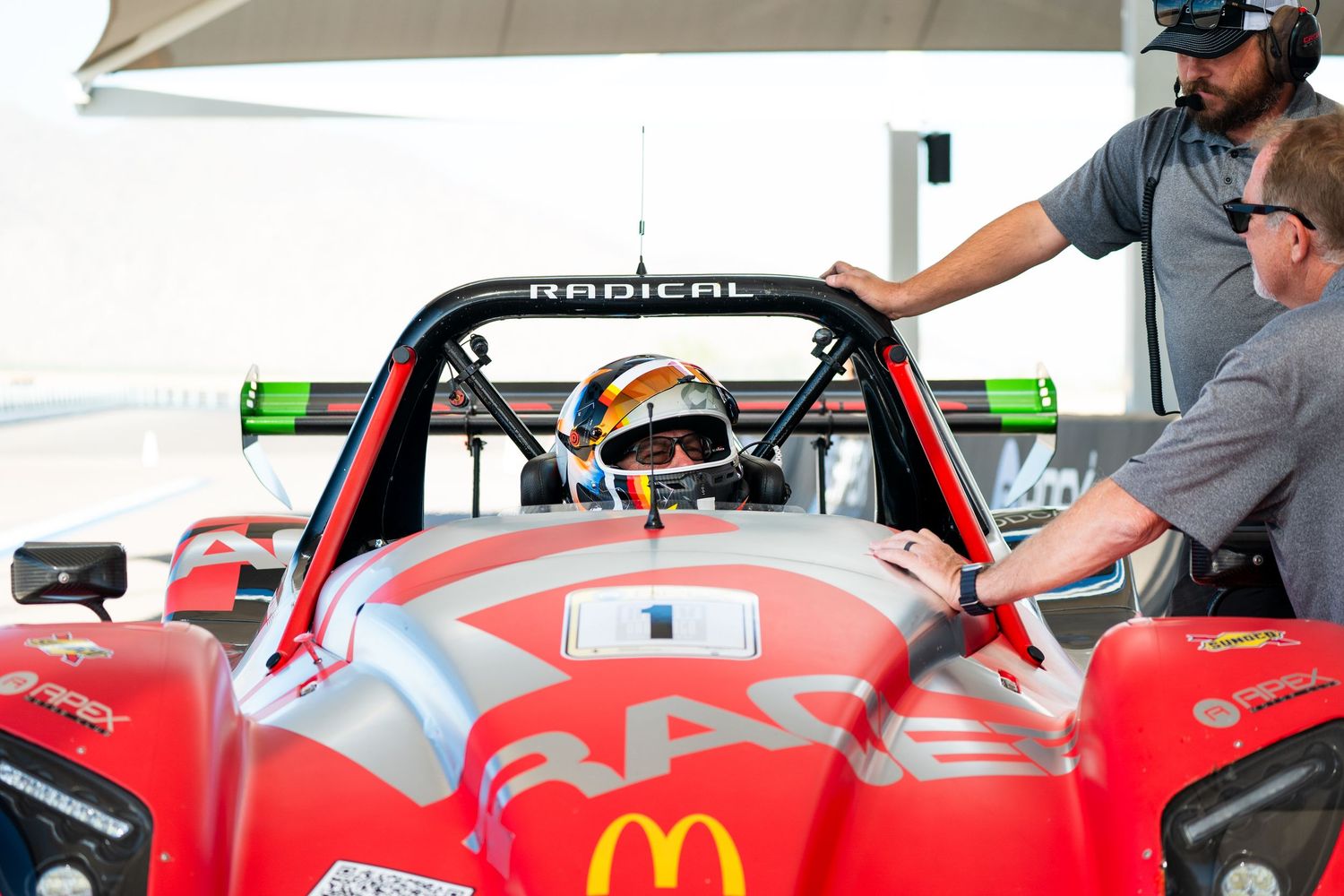 Red Formula racing car being adjusted in pit lane with crew members.