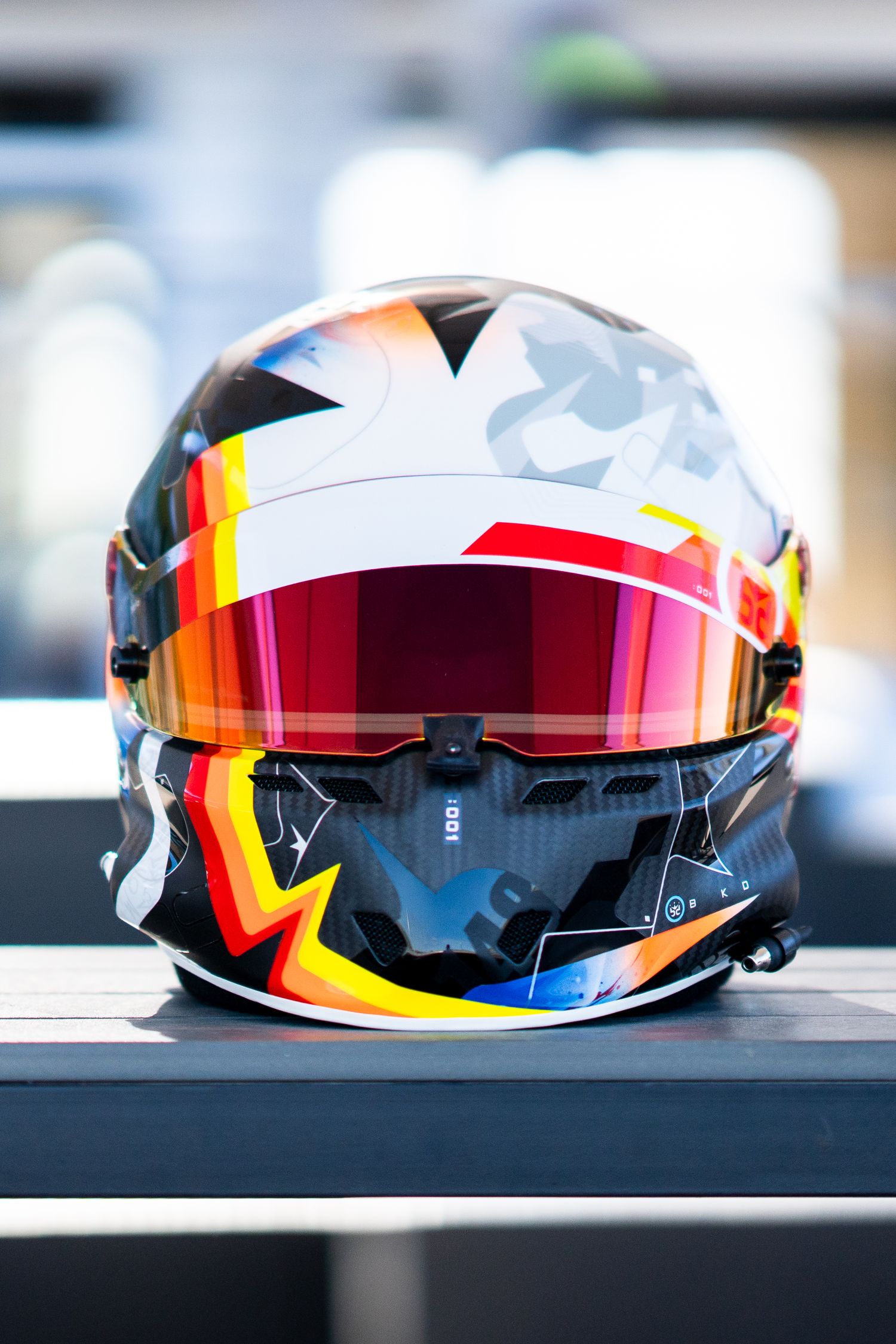 Racing helmet with vibrant multicolored geometric design and red visor displayed on dark surface.