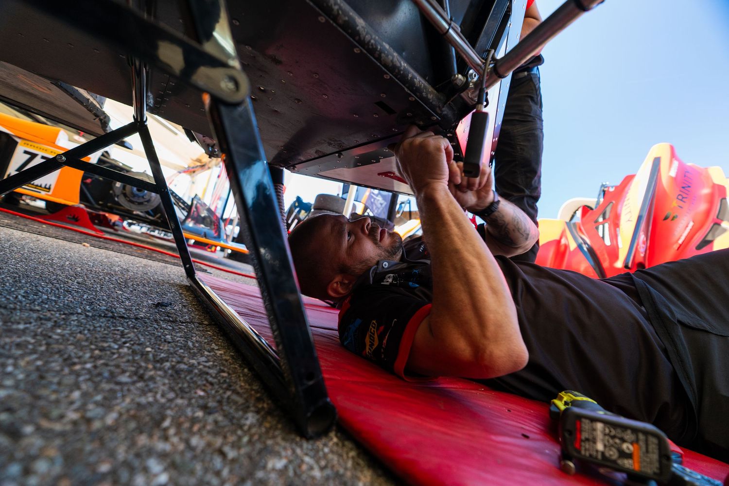 Detailed inspection being conducted underneath a race car on a lift.