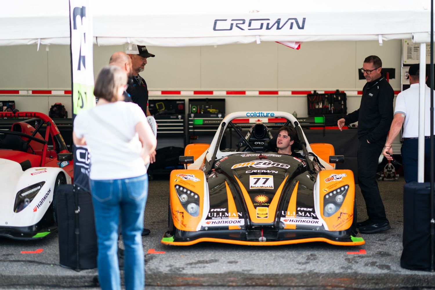 Row of yellow and orange Crown racing cars lined up in pit lane.