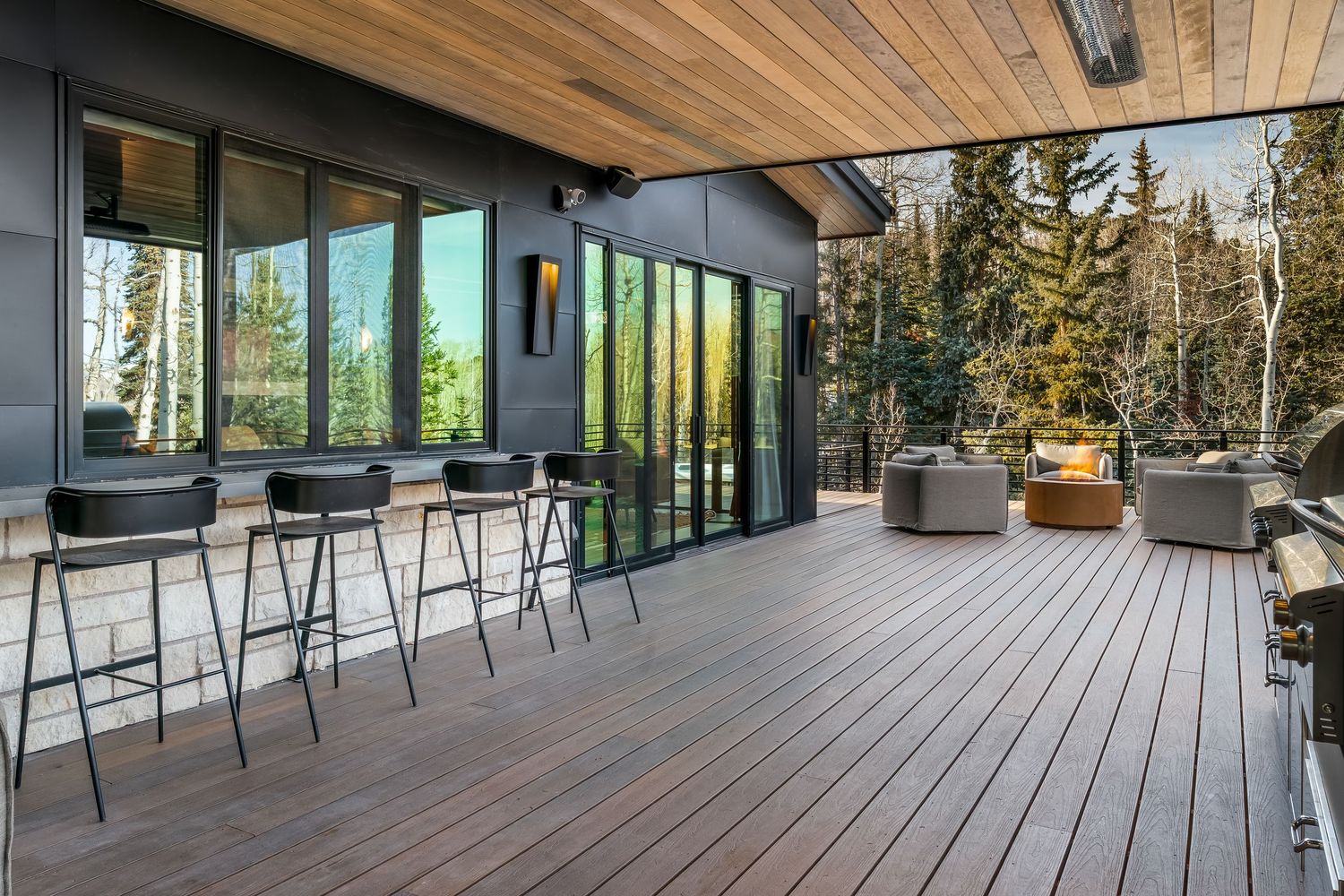 Contemporary deck space with wooden ceiling and glass railings overlooking a scenic forest landscape.