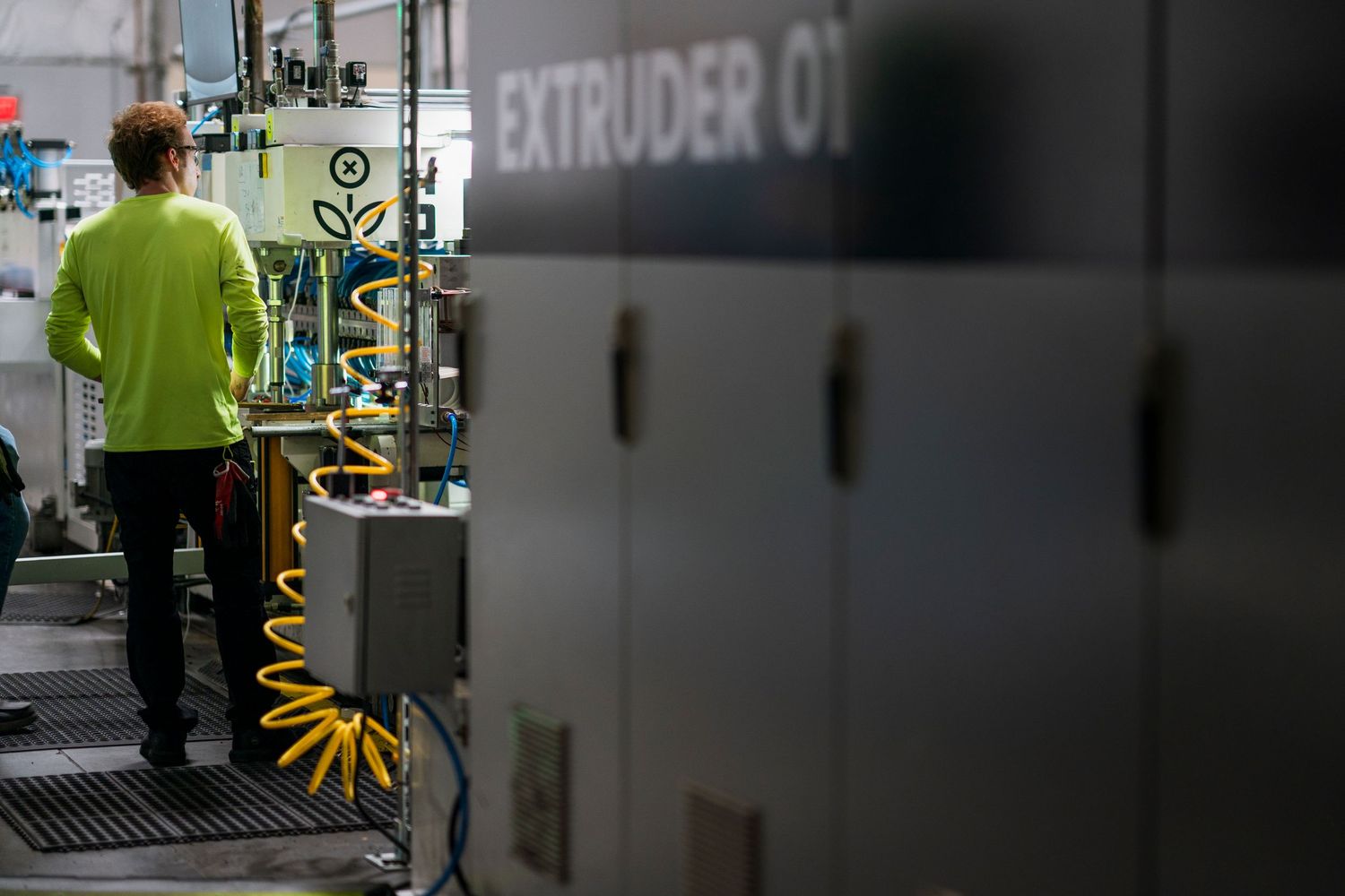 Industrial worker in safety vest operates machinery in a manufacturing facility with control panels and equipment.