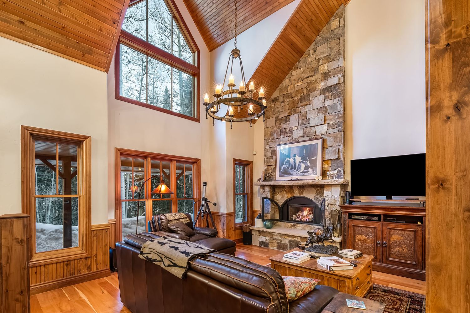 Open concept lodge interior featuring vaulted wood ceilings, large windows, and natural stone accents.