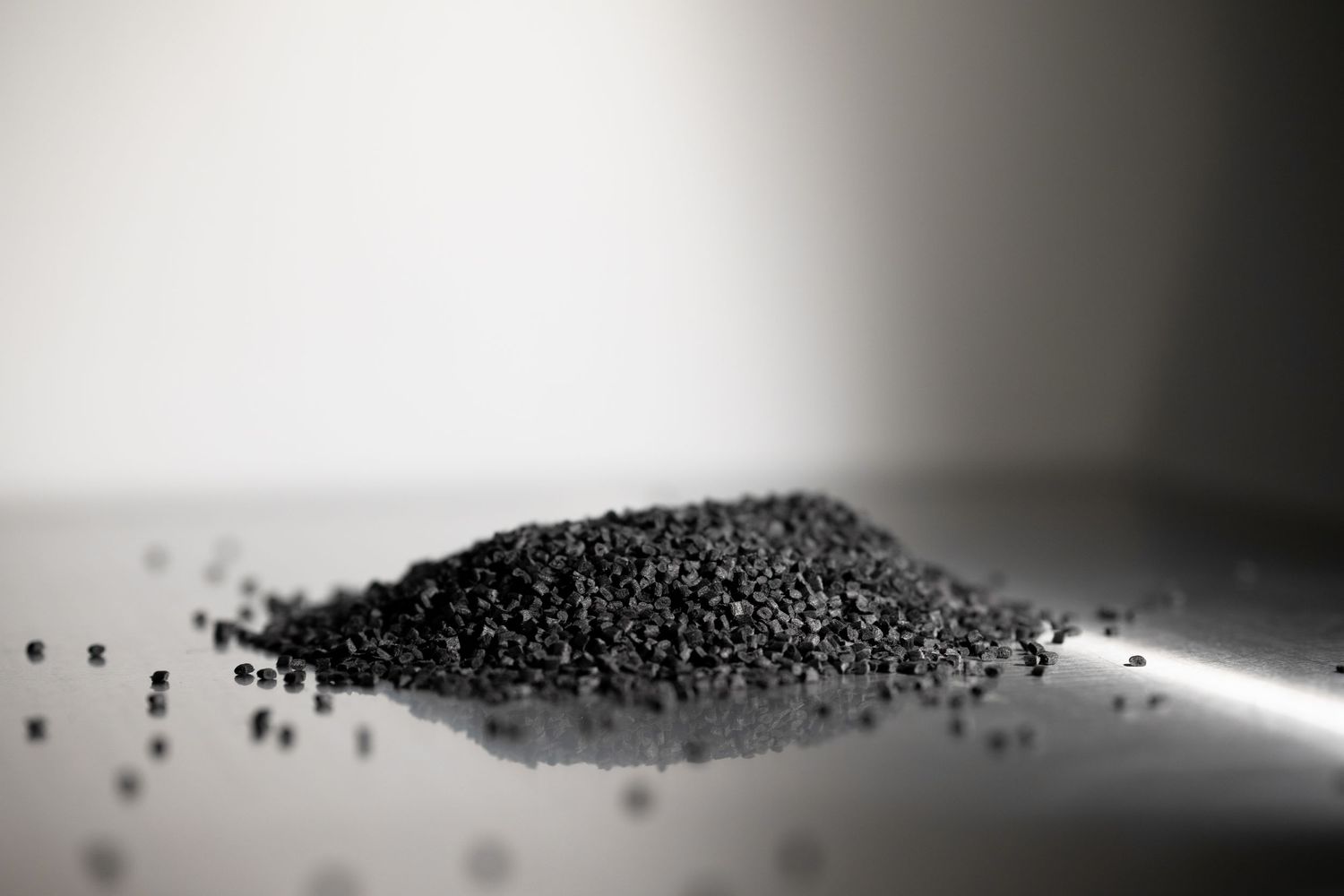 Black granular material scattered on reflective surface in monochrome.