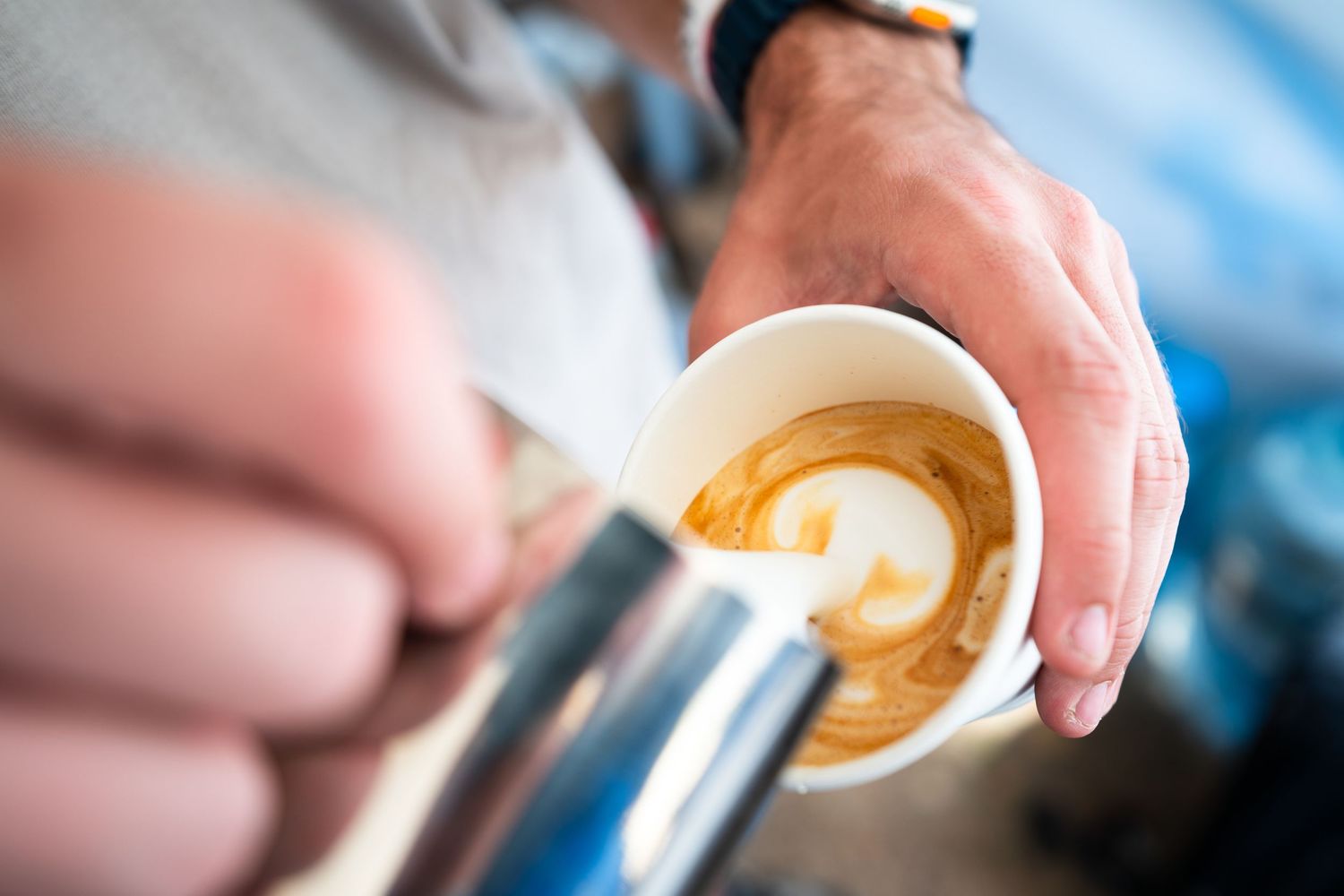 Barista pouring steamed milk to create latte art in a white cup at a coffee event.