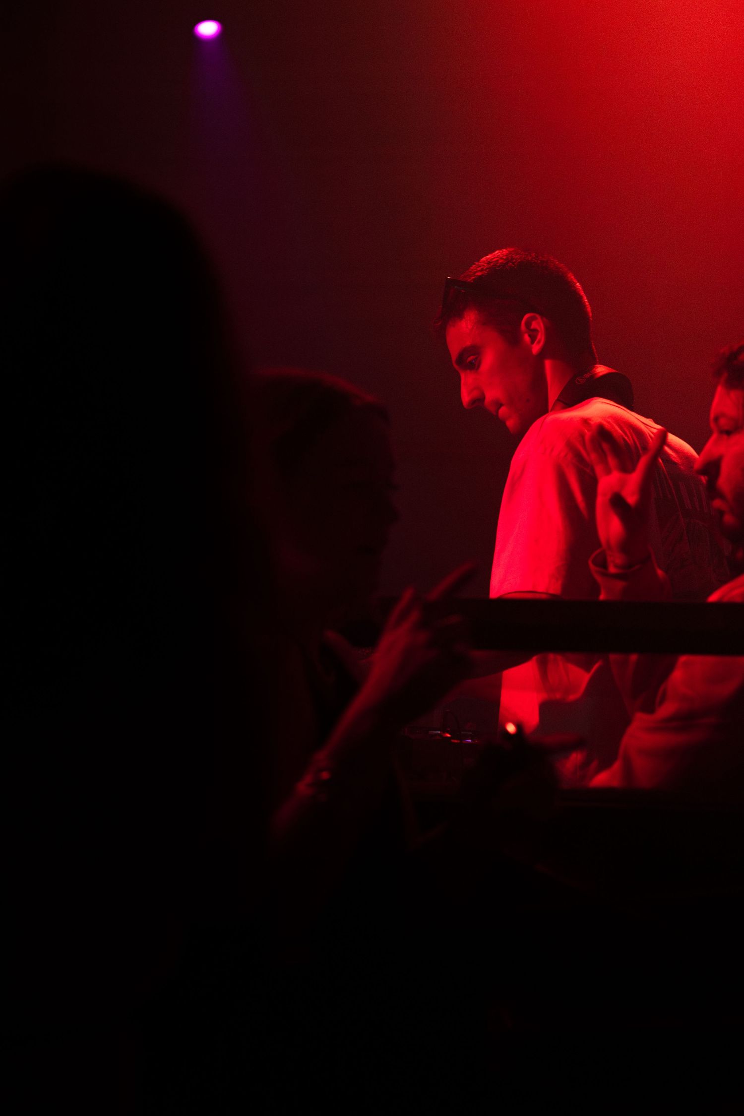 A performer illuminated by dramatic red stage lighting plays music at a dimly lit concert venue.